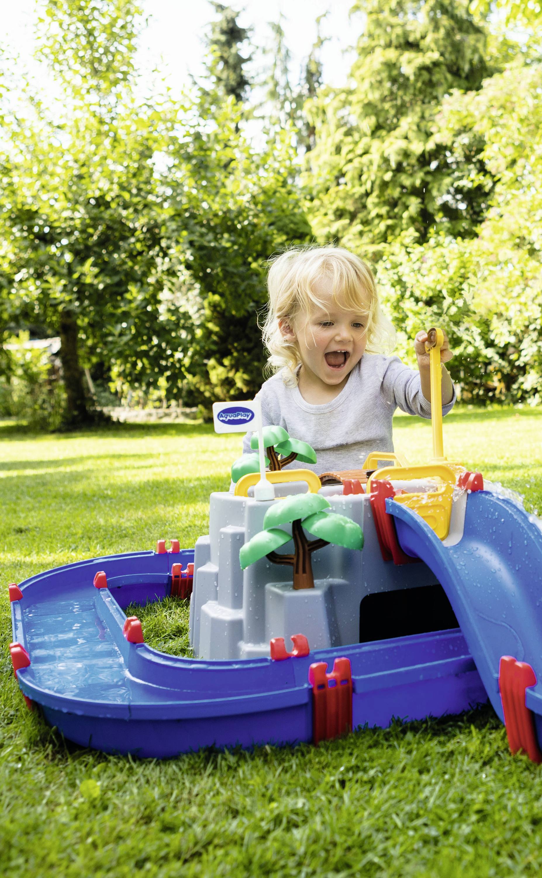 Un enfant joue joyeusement avec un jouet aquatique coloré dans le jardin. Des arbres et de l'herbe en arrière-plan.