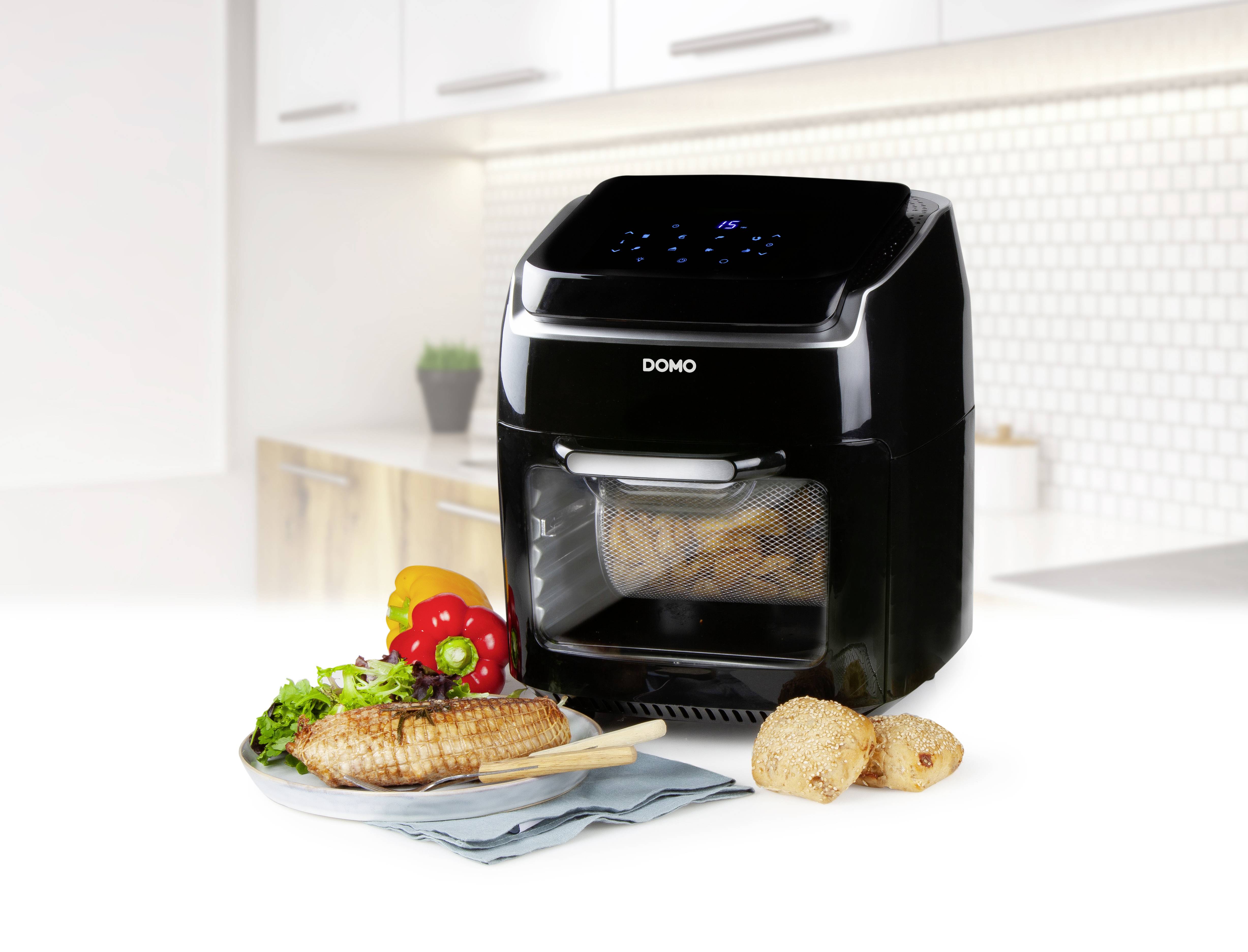 Friteuse à air chaud noir sur un plan de travail de cuisine, à côté d'un repas servi avec de la viande grillée, des légumes et un pain.
