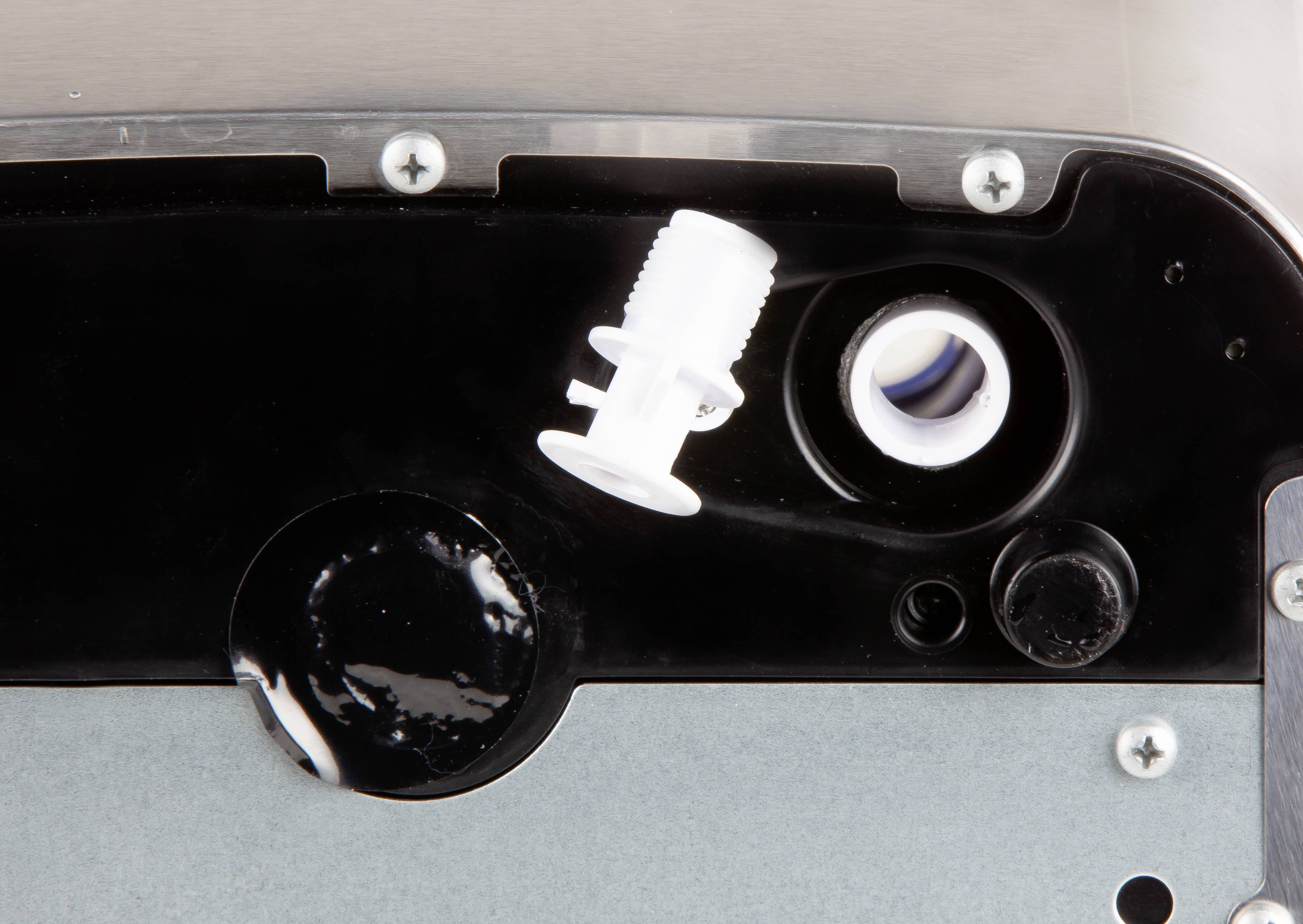 Gros plan d'une pièce mécanique avec un embout en plastique blanc en saillie et plusieurs vis sur une plaque métallique.