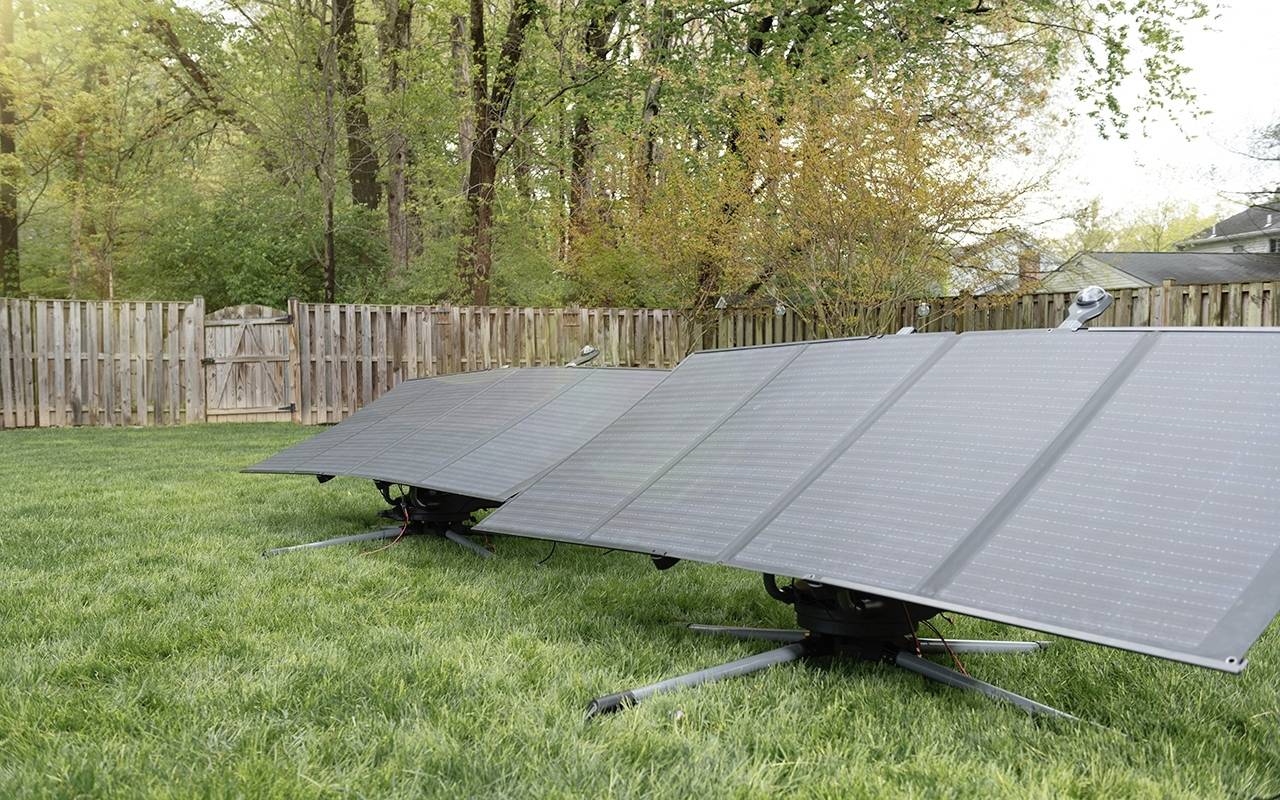 Trois panneaux solaires sont installés sur une pelouse dans un jardin, entourés d'une clôture en bois et d'arbres en arrière-plan.