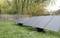 Trois panneaux solaires sont installés sur une pelouse dans un jardin, entourés d'une clôture en bois et d'arbres en arrière-plan.