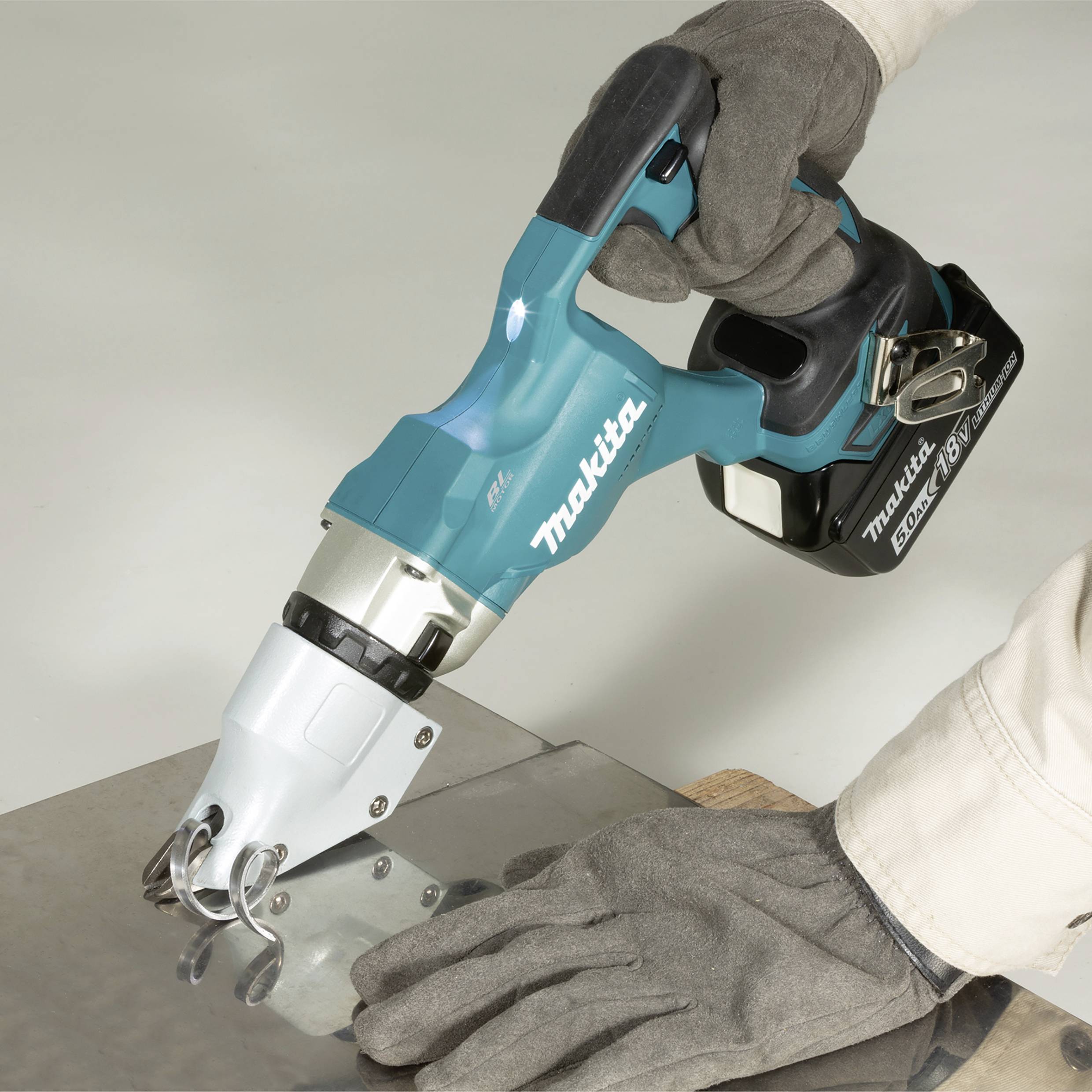Cisaille à batterie de Makita coupe à travers une plaque métallique. Porter des gants, la main tient l'outil en toute sécurité.
