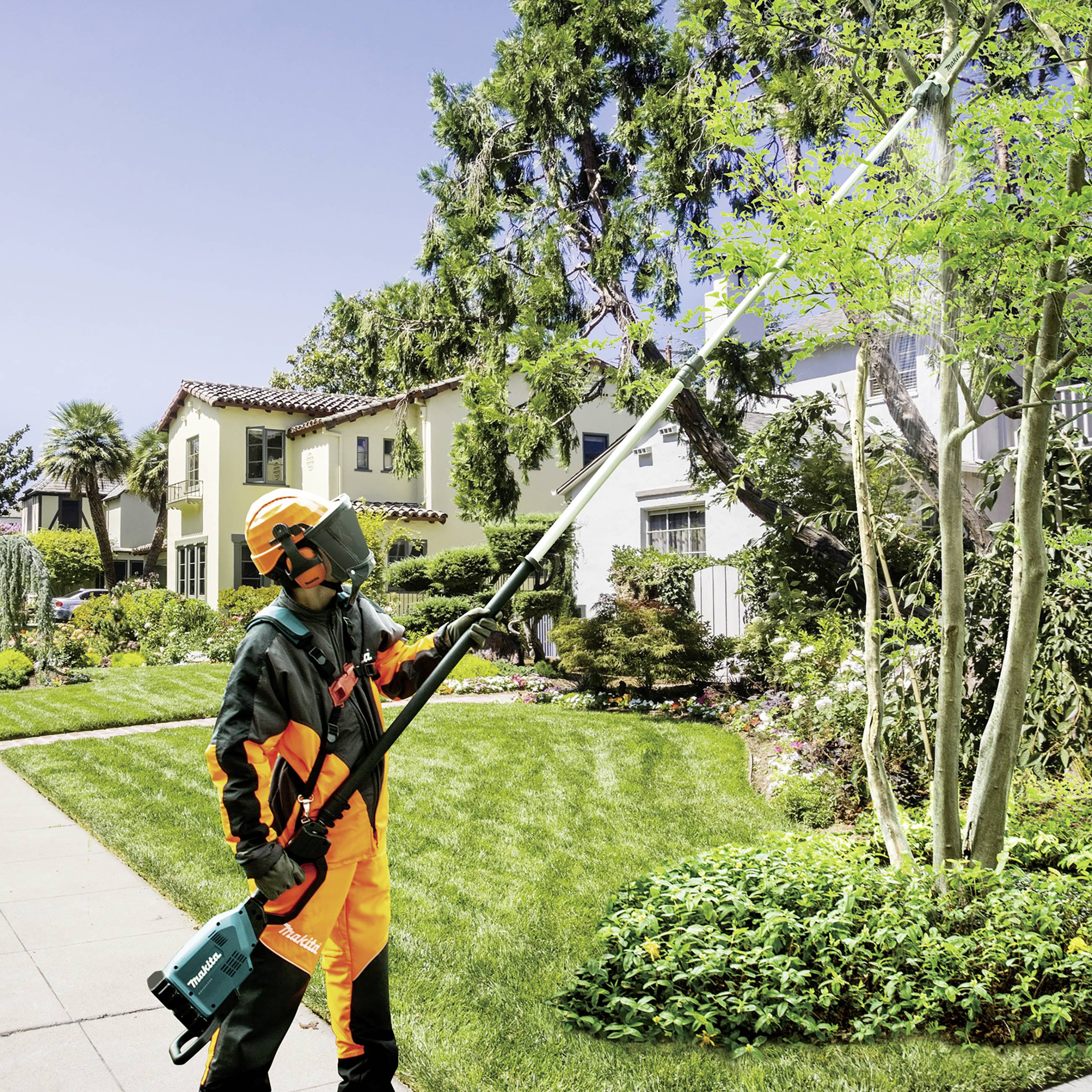 Une personne portant un équipement de protection coupe des branches à l'aide d'un taille-haie électrique sur un arbre dans un jardin bien entretenu.