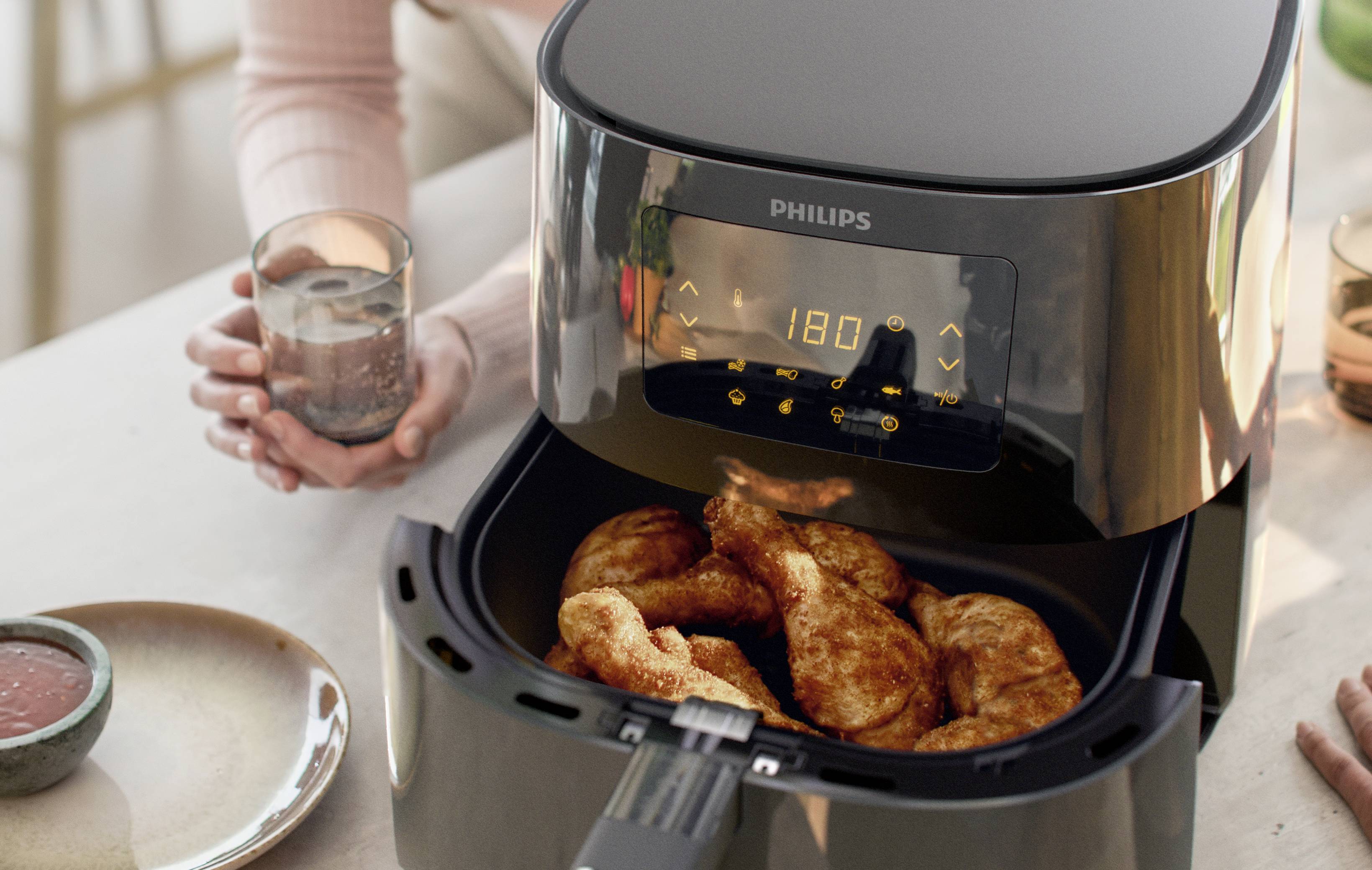 Une personne utilise une friteuse à air chaud pour préparer des pilons de poulet. L'affichage indique 180 degrés Celsius.