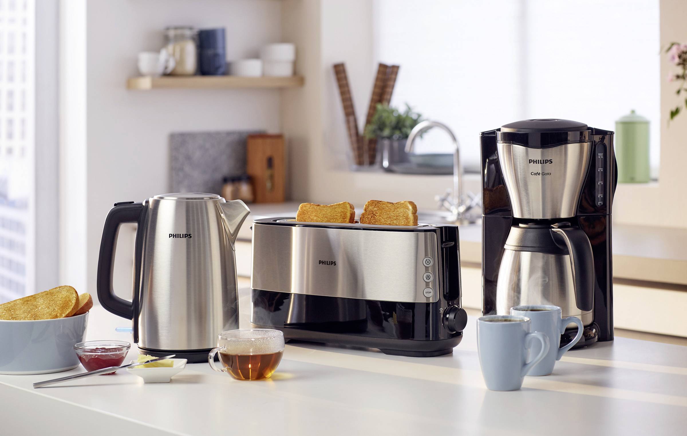 Un espace de travail de cuisine moderne avec une bouilloire, un grille-pain à deux tranches et une machine à café à côté de tasses.
