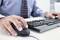 Une personne en tenue formelle utilise une souris d'ordinateur et tape sur un clavier à un bureau.