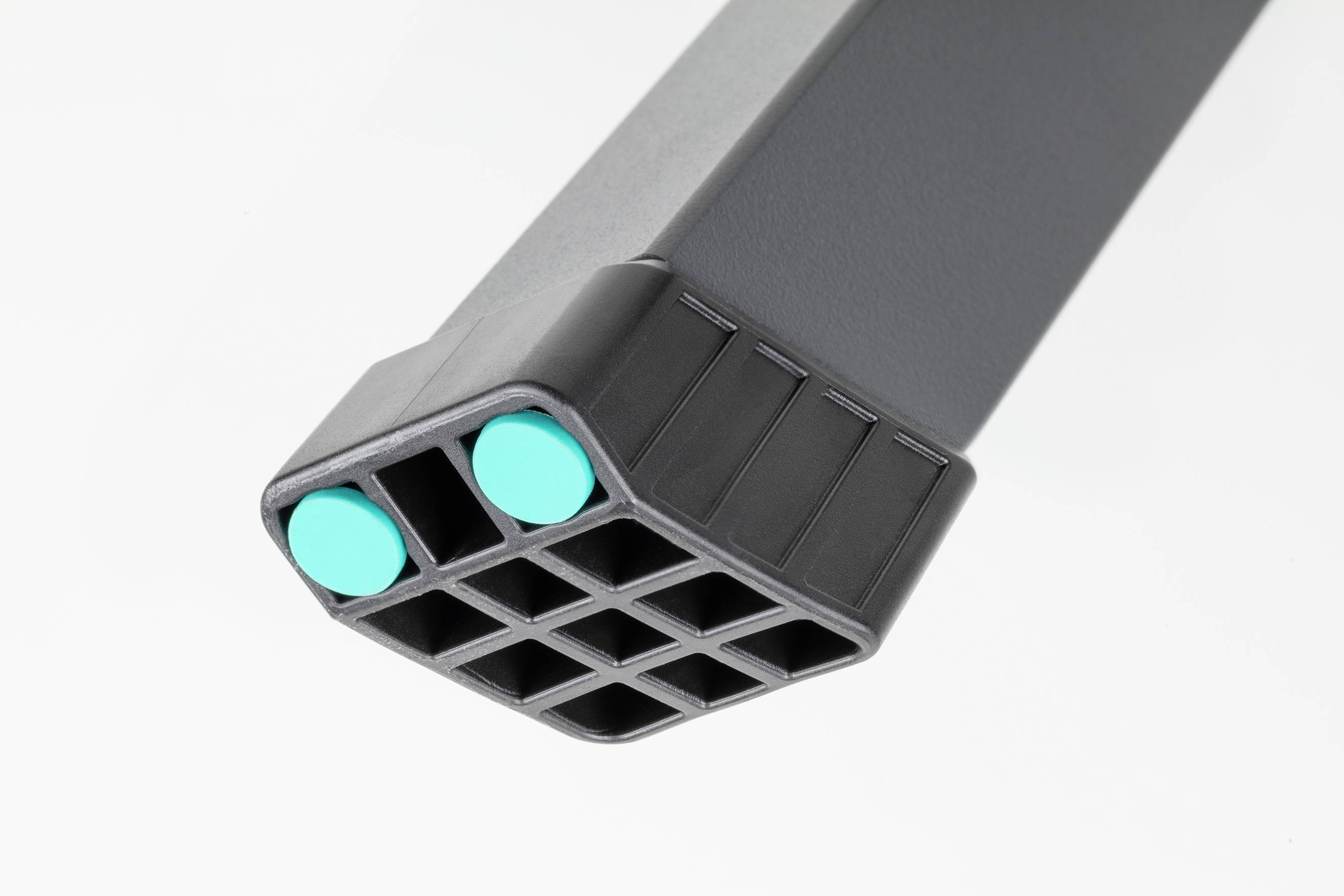Un prolongement de pied de table rectangulaire gris avec une extrémité en plastique antidérapant et deux pastilles turquoises sur sa face inférieure.