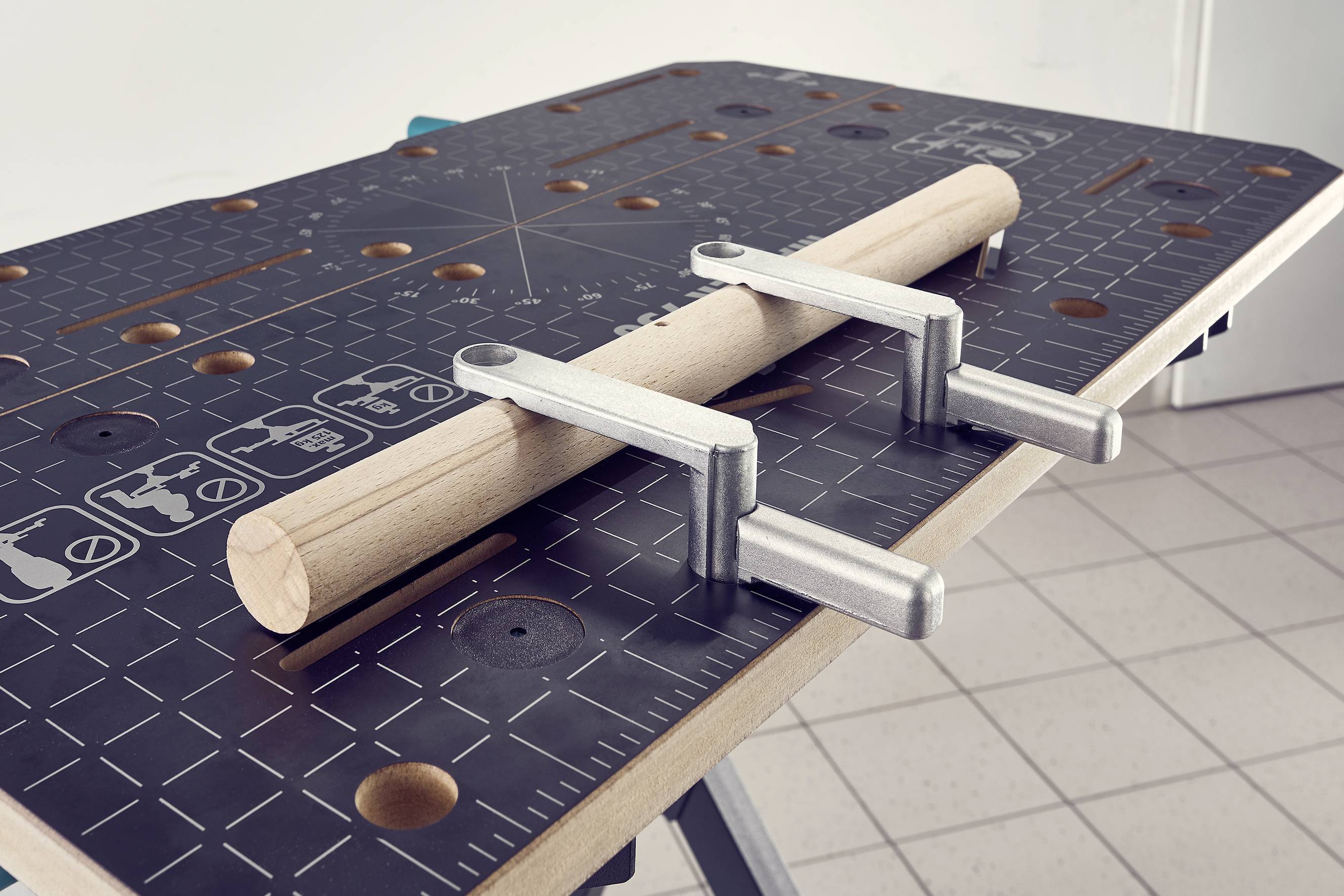 Un cylindre en bois est fixé sur un établi à l'aide d'un dispositif de serrage. La surface est marquée de motifs géométriques.
