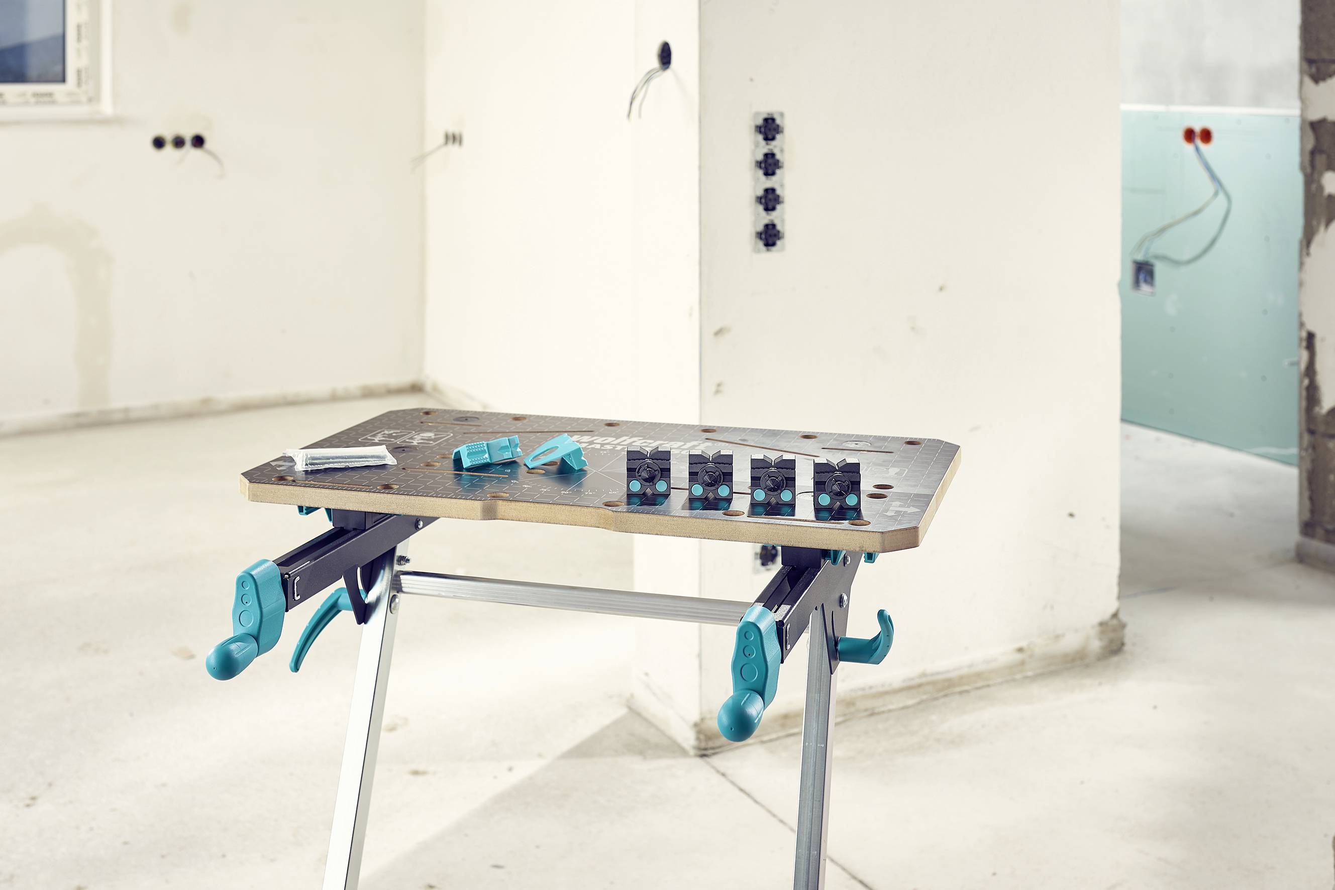 Une table avec des outils sur un chantier, des câbles sortant des murs en arrière-plan. Des travaux de rénovation sont en cours.