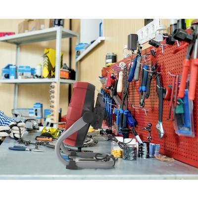Une table d'atelier bien éclairée avec une imprimante 3D au premier plan. Sur le mur sont accrochés divers outils soigneusement rangés.