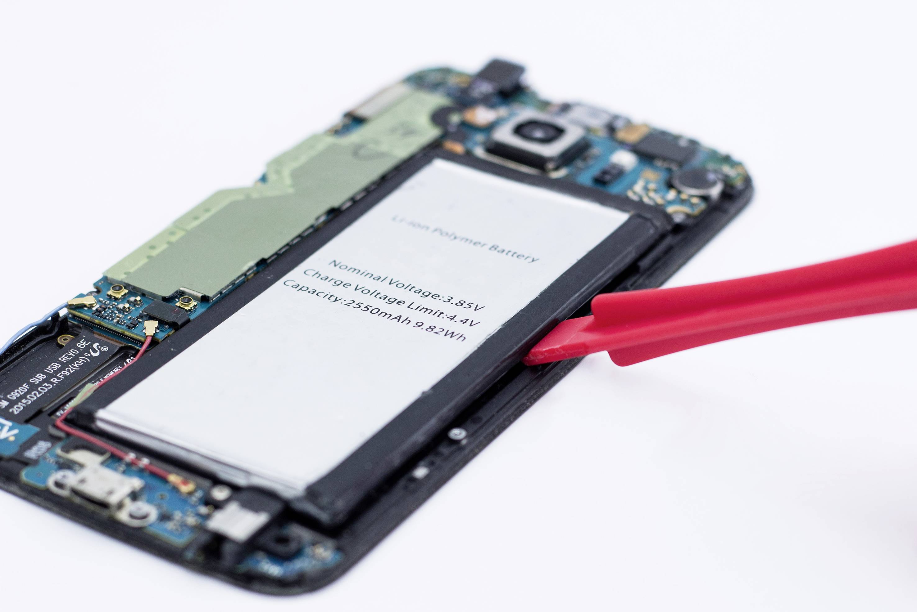 Smartphone ouvert, montrant la batterie lithium-polymère exposée avec un outil de levier rouge pour son retrait.