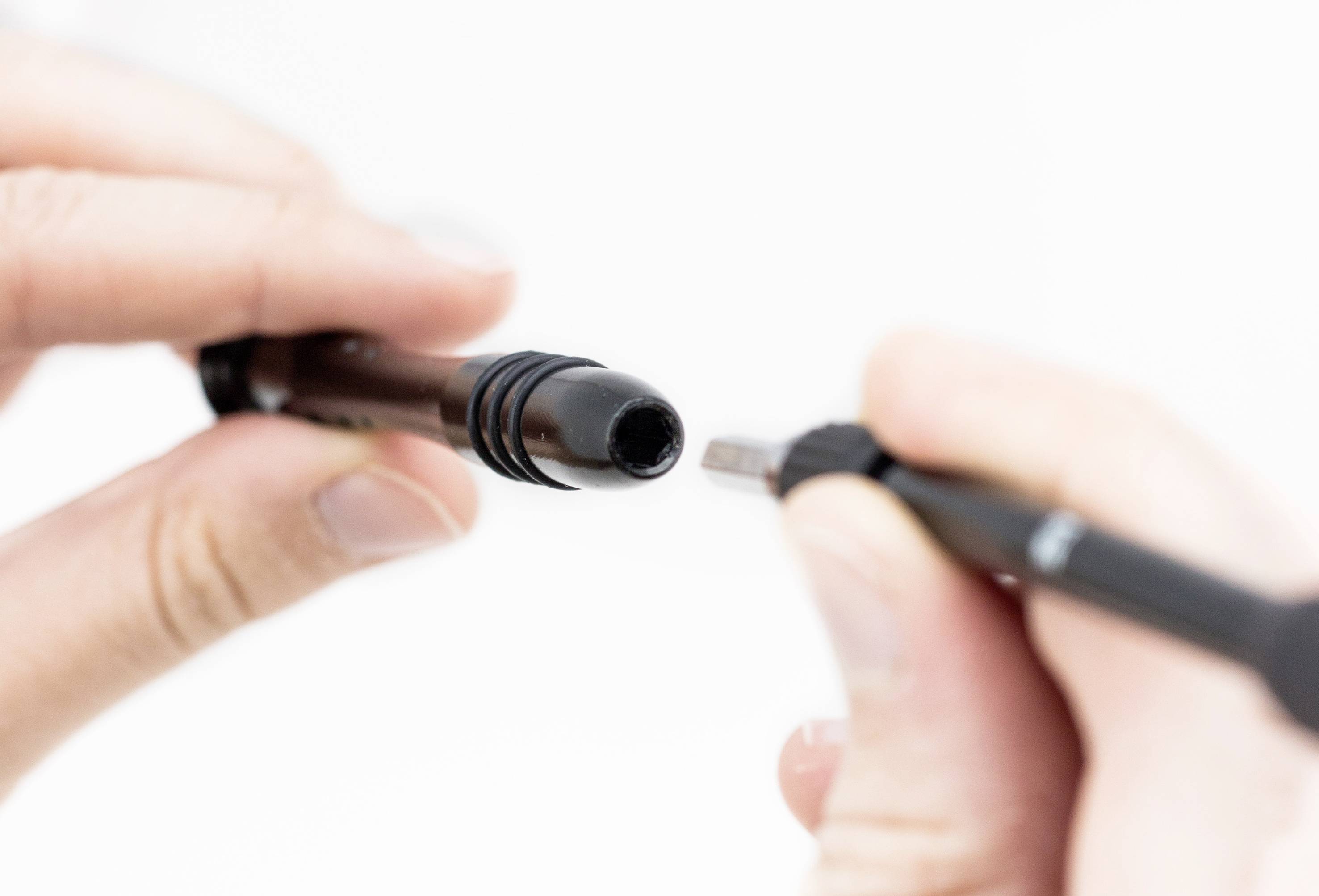 Une main tient un stylo, tandis que l'autre main insère une pointe pour l'échange. Gros plan, focus sur le stylo.