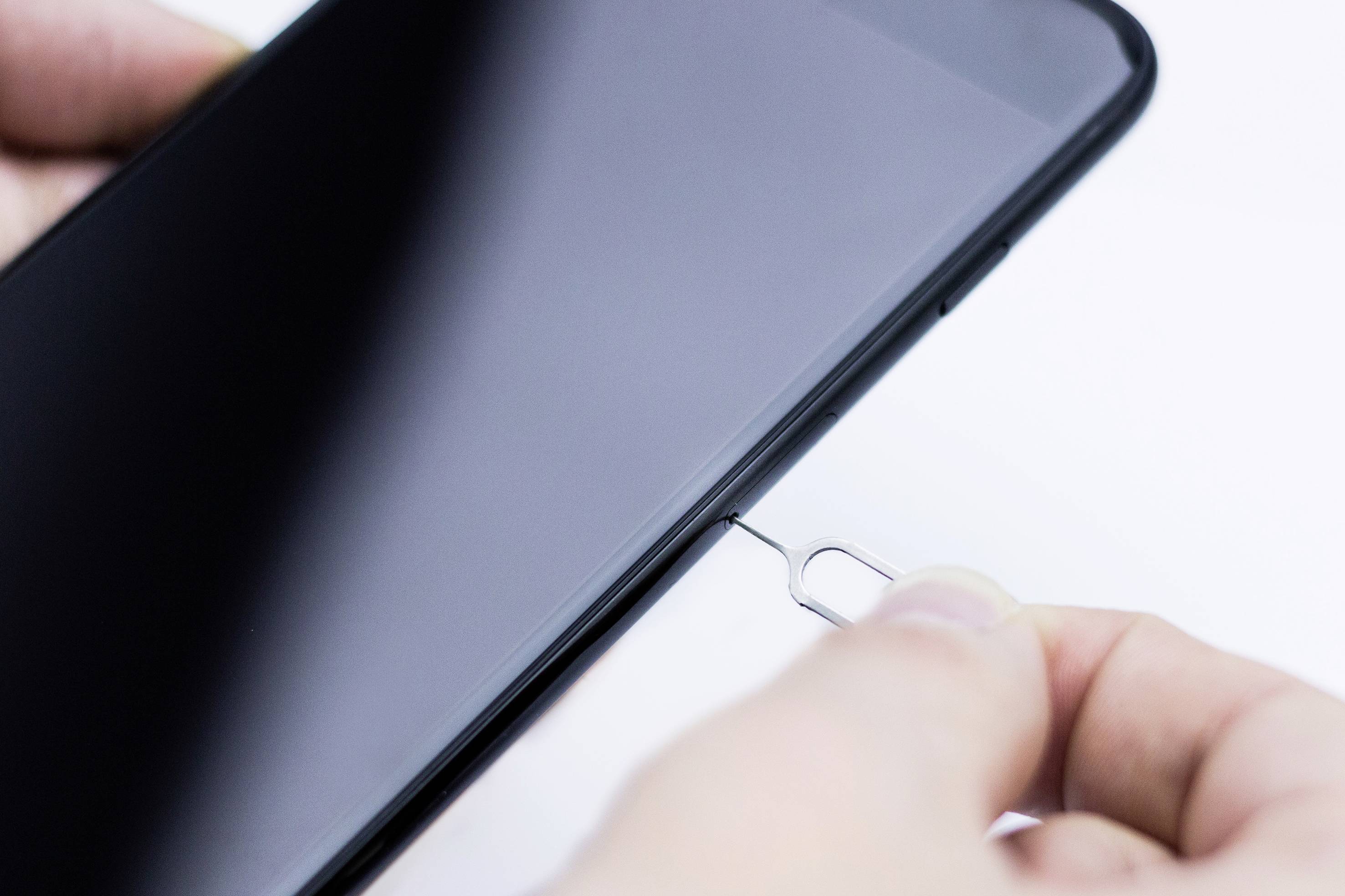Une main insère un outil d'éjection de carte SIM dans le tiroir pour carte SIM d'un smartphone.