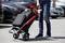 Une personne pousse un chariot de courses noir sur un parking. Dans le chariot se trouvent des radis frais et du poireau.