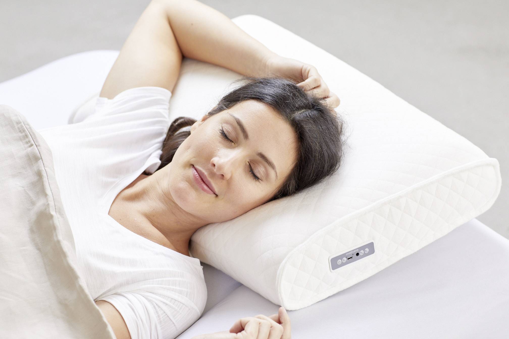 Une femme est allongée dans son lit et dort sur un oreiller blanc. Elle semble détendue, avec un léger sourire aux lèvres.
