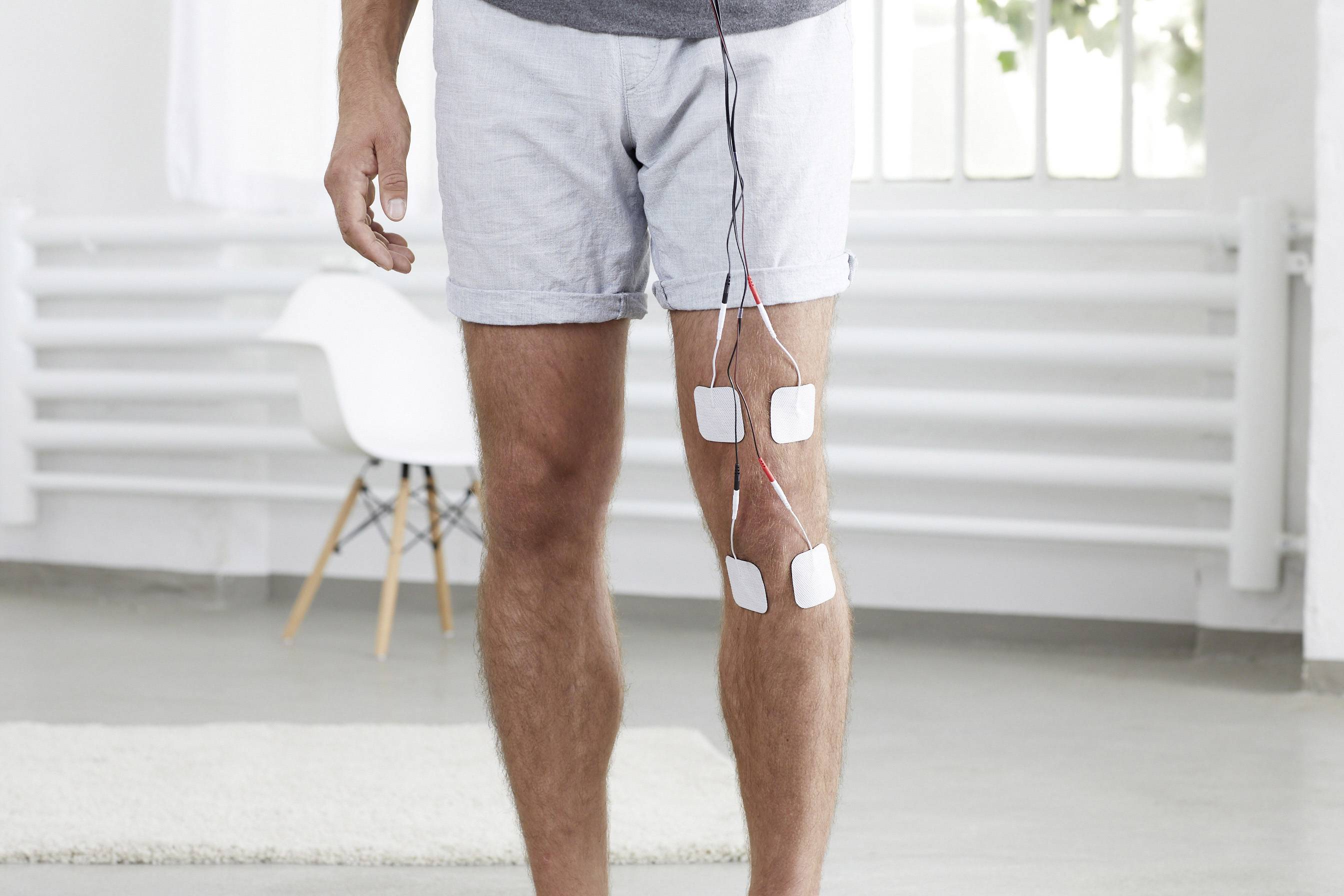 Une personne se tient dans une pièce lumineuse avec des électrodes de stimulation électrique attachées à sa cuisse.