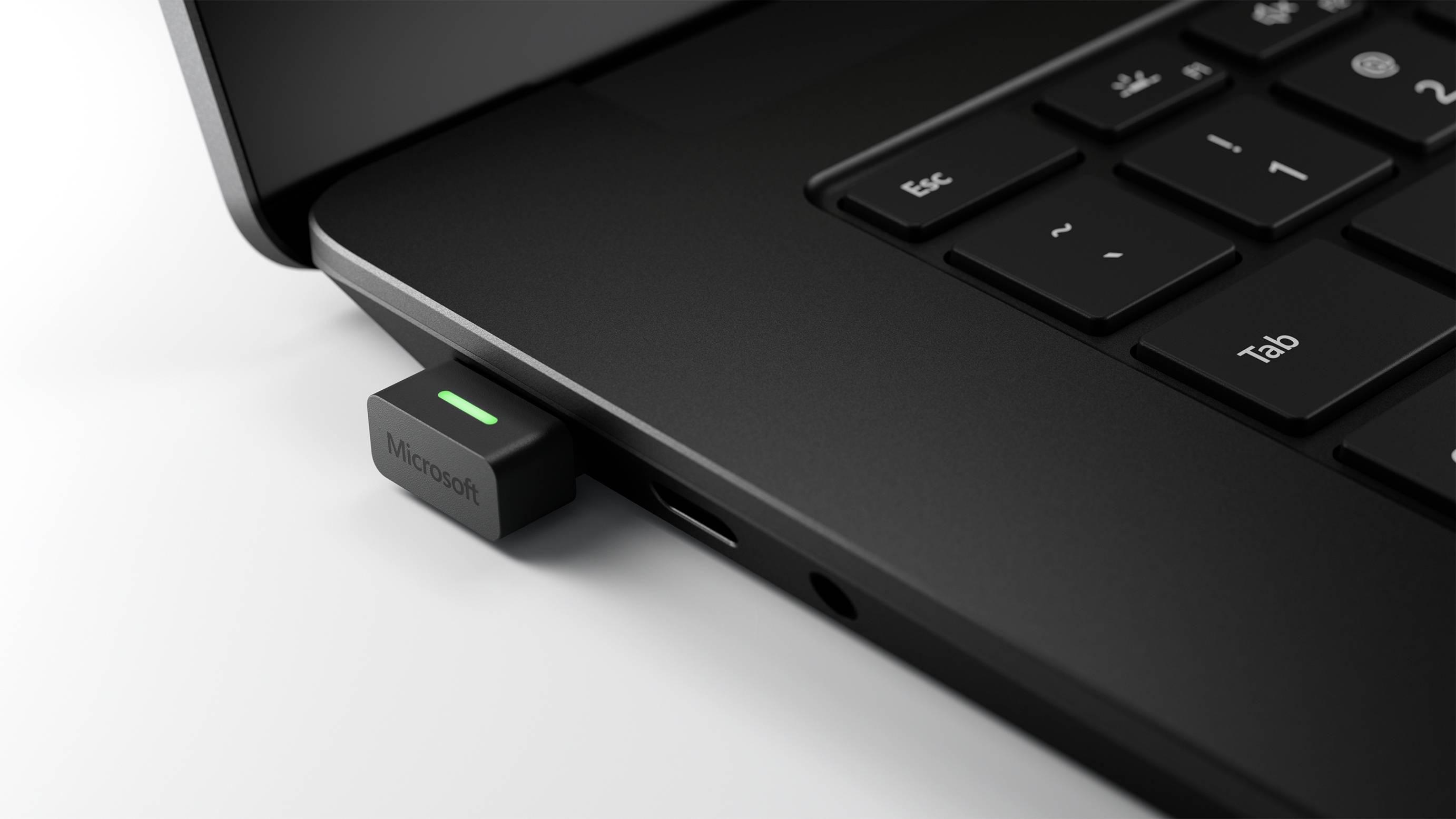 Une clé USB noire avec un voyant vert est branchée dans un ordinateur portable posé sur une surface blanche.