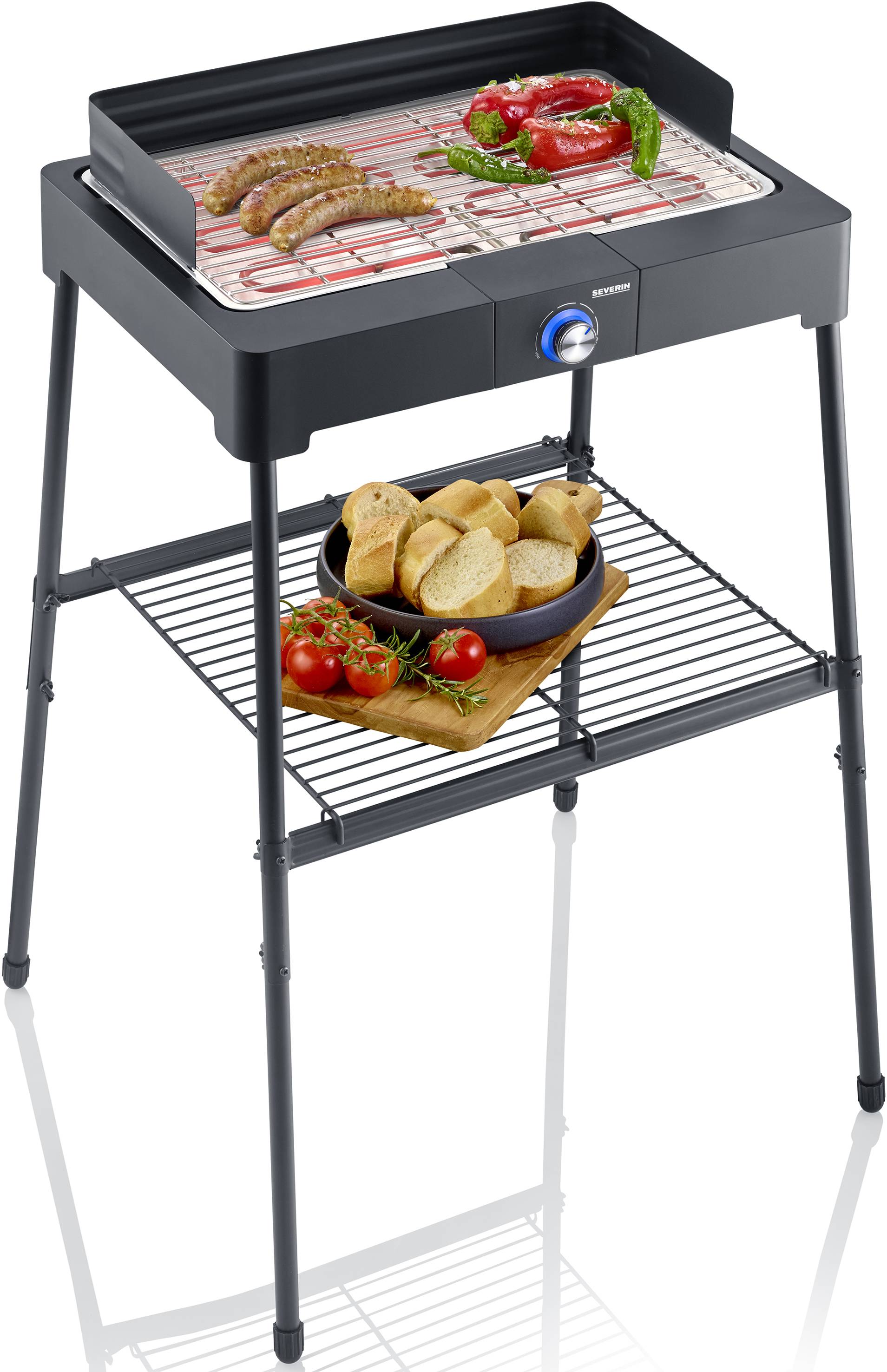 Un grill électrique avec des saucisses et des légumes sur la grille, accompagné de pain et de tomates sur la table en dessous.