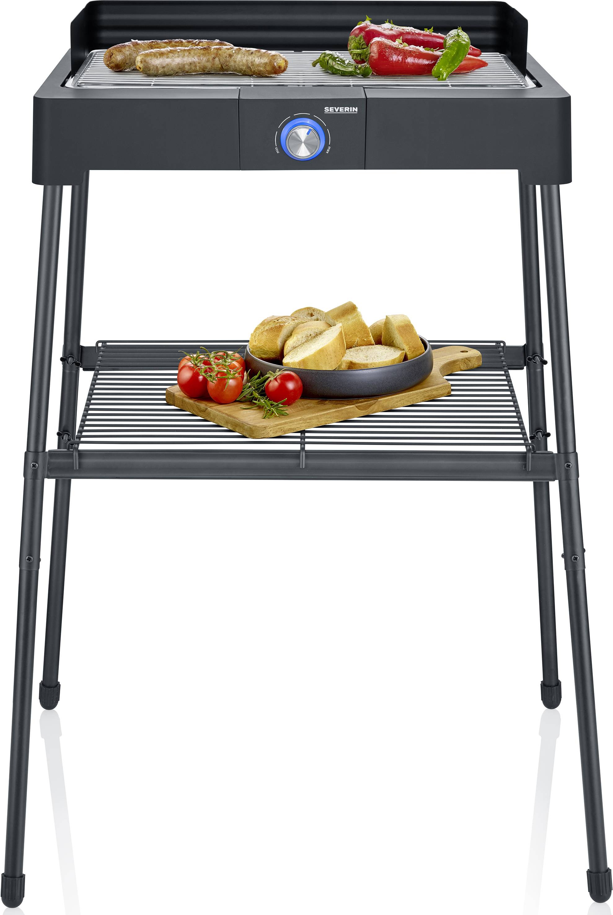 Un grill électrique avec une saucisse et des légumes sur la surface de cuisson. En-dessous, une grille avec du pain et des tomates. Le grill a quatre pieds.
