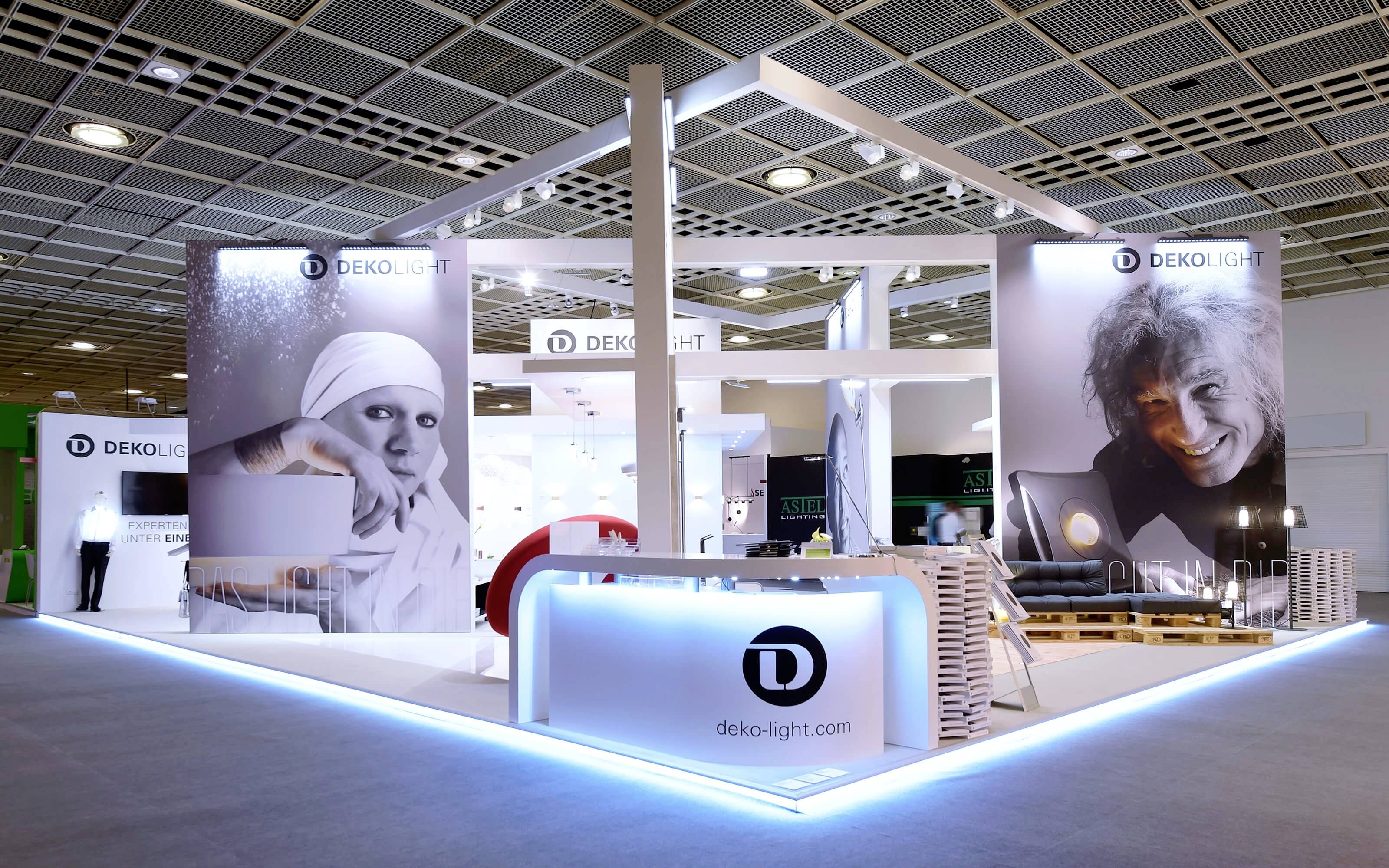 Un stand d'exposition de l'entreprise 'Deko-Light' présente des solutions d'éclairage modernes. De grandes bannières avec un comptoir éclairé et le logo au premier plan.