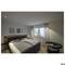 Une chambre avec un lit double, des tables de chevet, trois tableaux encadrés au mur, une fenêtre équipée de stores vénitiens et un fauteuil.