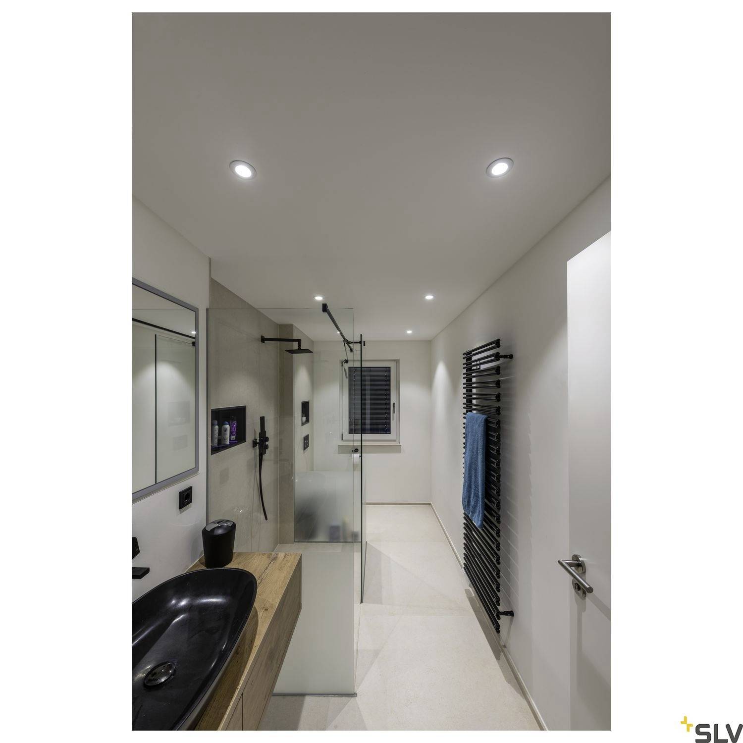 Salle de bain moderne avec un lavabo noir sur une tablette en bois, une cabine de douche en verre et un porte-serviettes avec une serviette bleue.