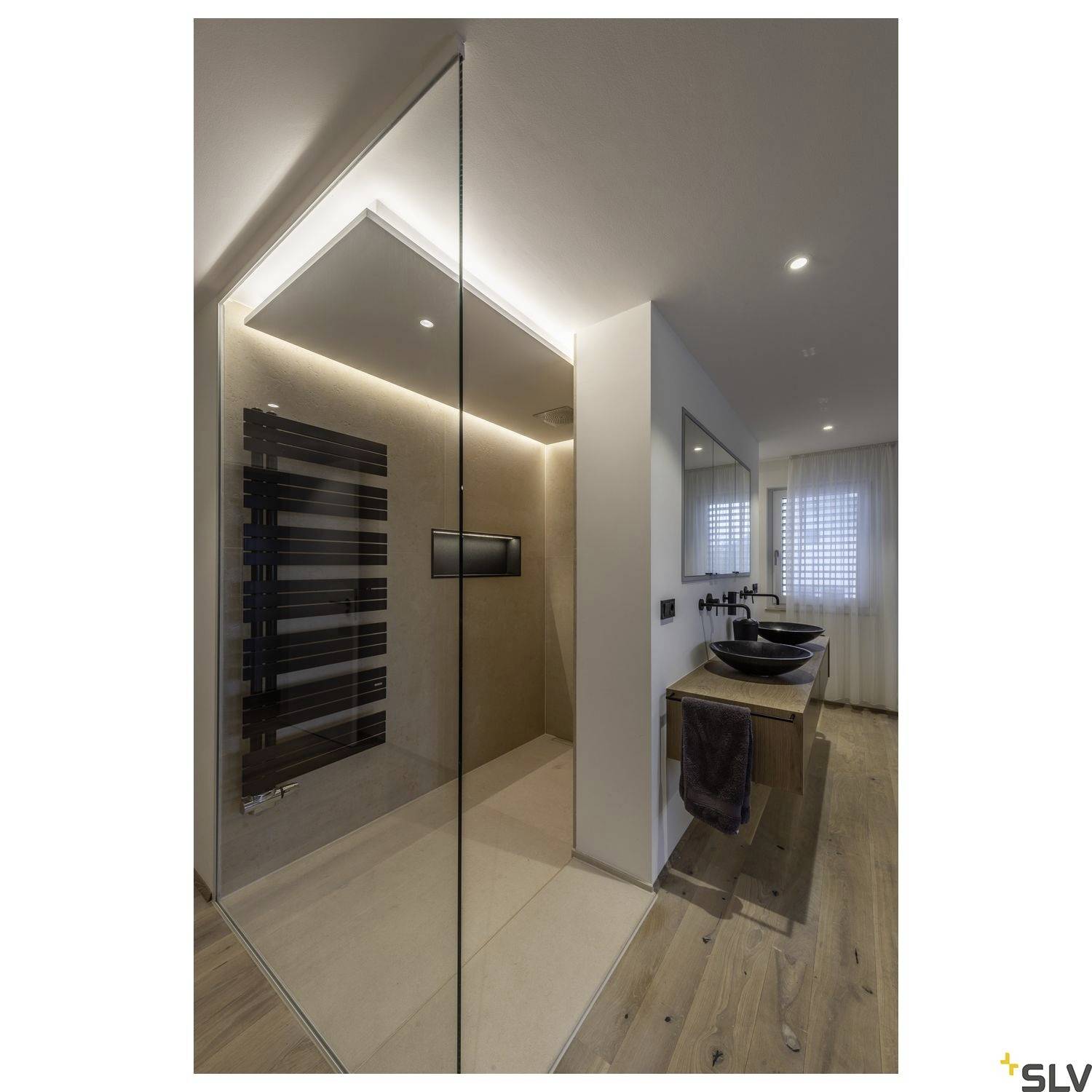 Salle de bain moderne avec douche en verre à l'italienne, sol en bois, deux lavabos et miroir éclairé. Design épuré et élégant.