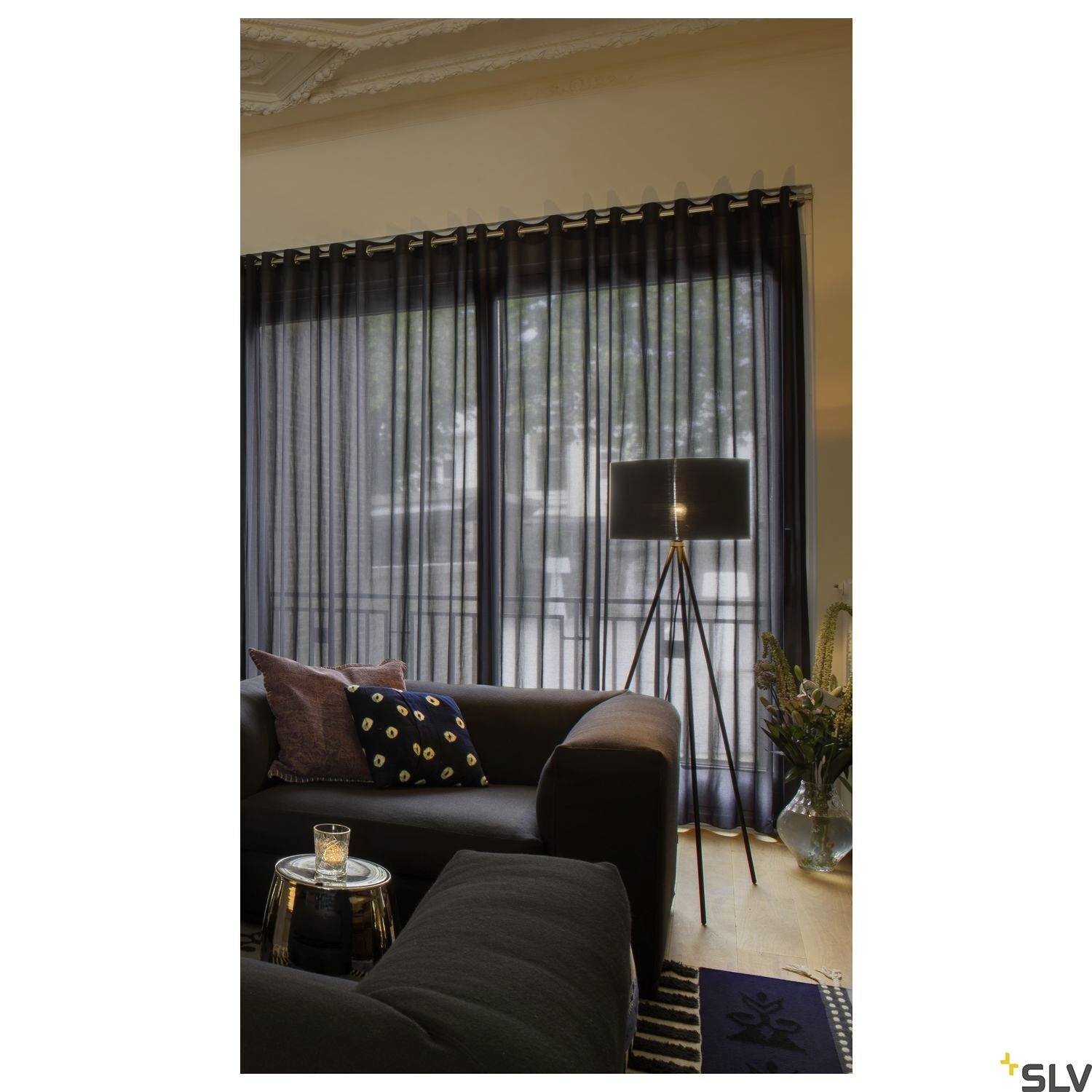 Une vue élégante d'un salon avec un canapé et un lampadaire à côté d'une fenêtre ornée de longs rideaux sombres.