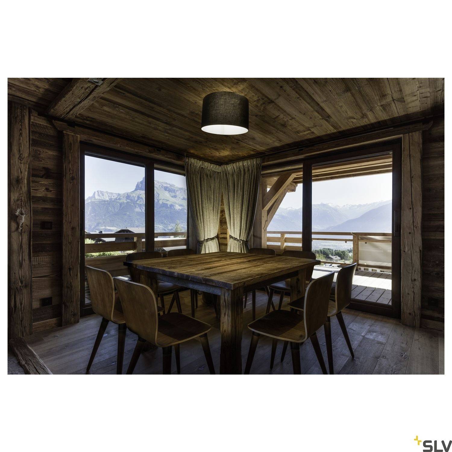 Un espace rustique aux murs et meubles en bois. Une table avec six chaises est placée devant une baie vitrée qui donne sur des montagnes.