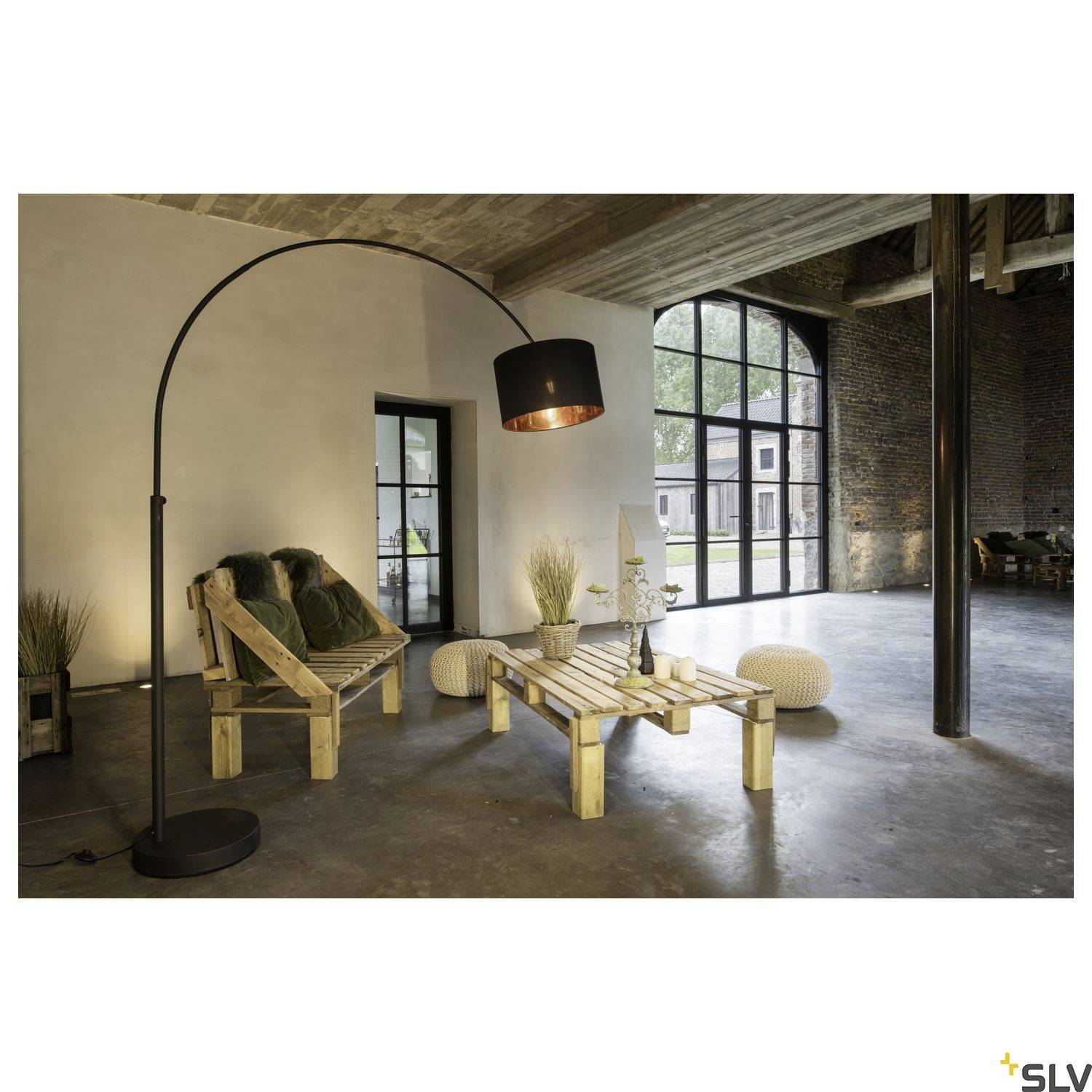 Salon moderne avec lampadaire, canapés en bois et table basse en palettes de bois. De grandes fenêtres offrent une vue sur le jardin.