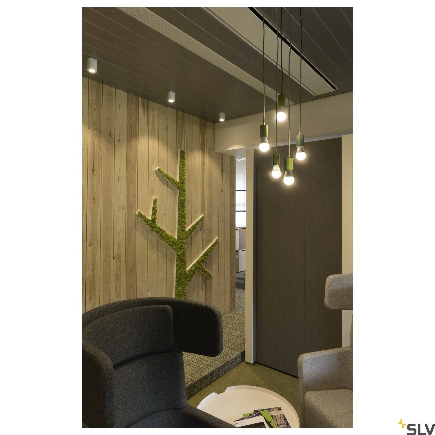 Espace de bureau moderne avec un mur en bois, une décoration de mousse verte en forme d'arbre, plusieurs lampes suspendues et un fauteuil gris. Aménagé de manière accueillante et élégante.