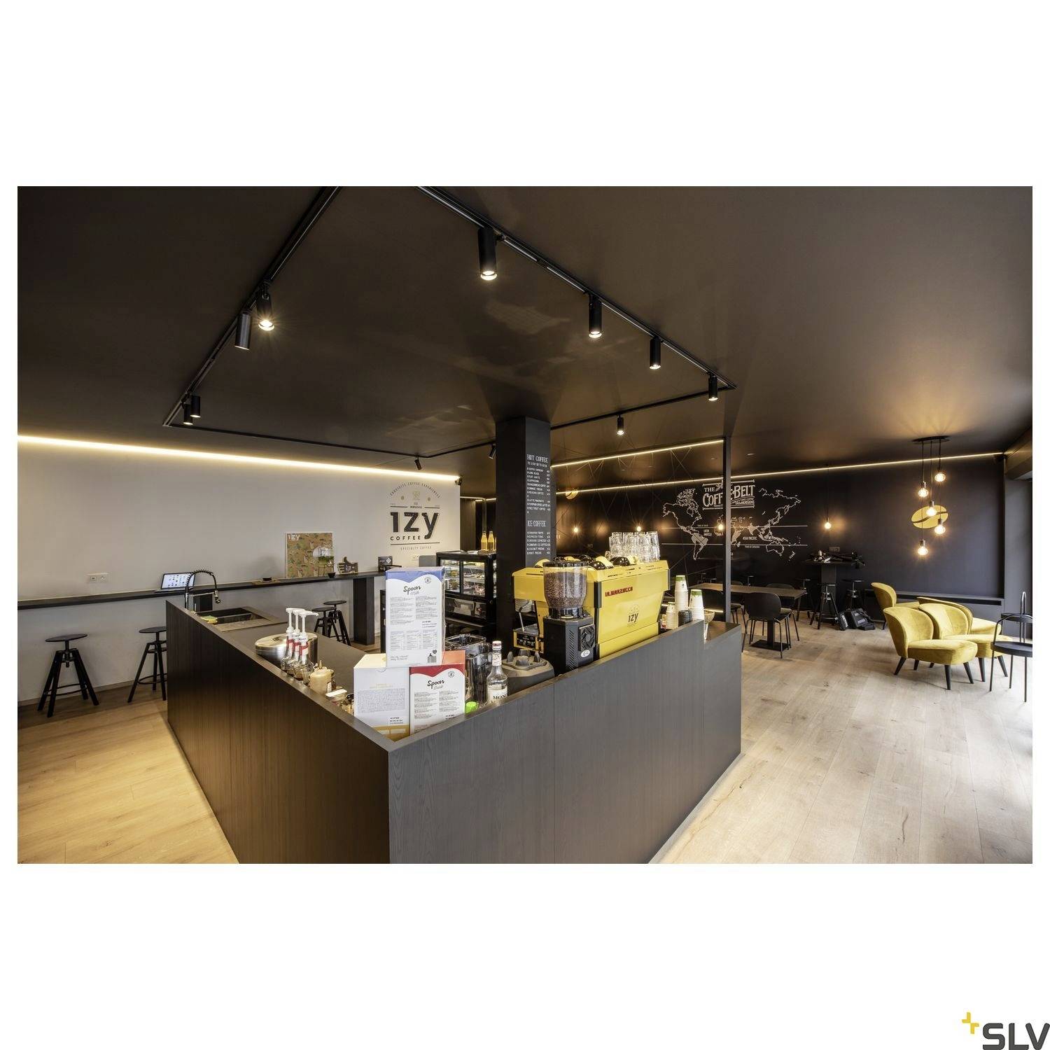 Café moderne avec sol en bois, plafonds noirs et éléments d'éclairage sur rail. Machine à café jaune sur le comptoir, sièges confortables.