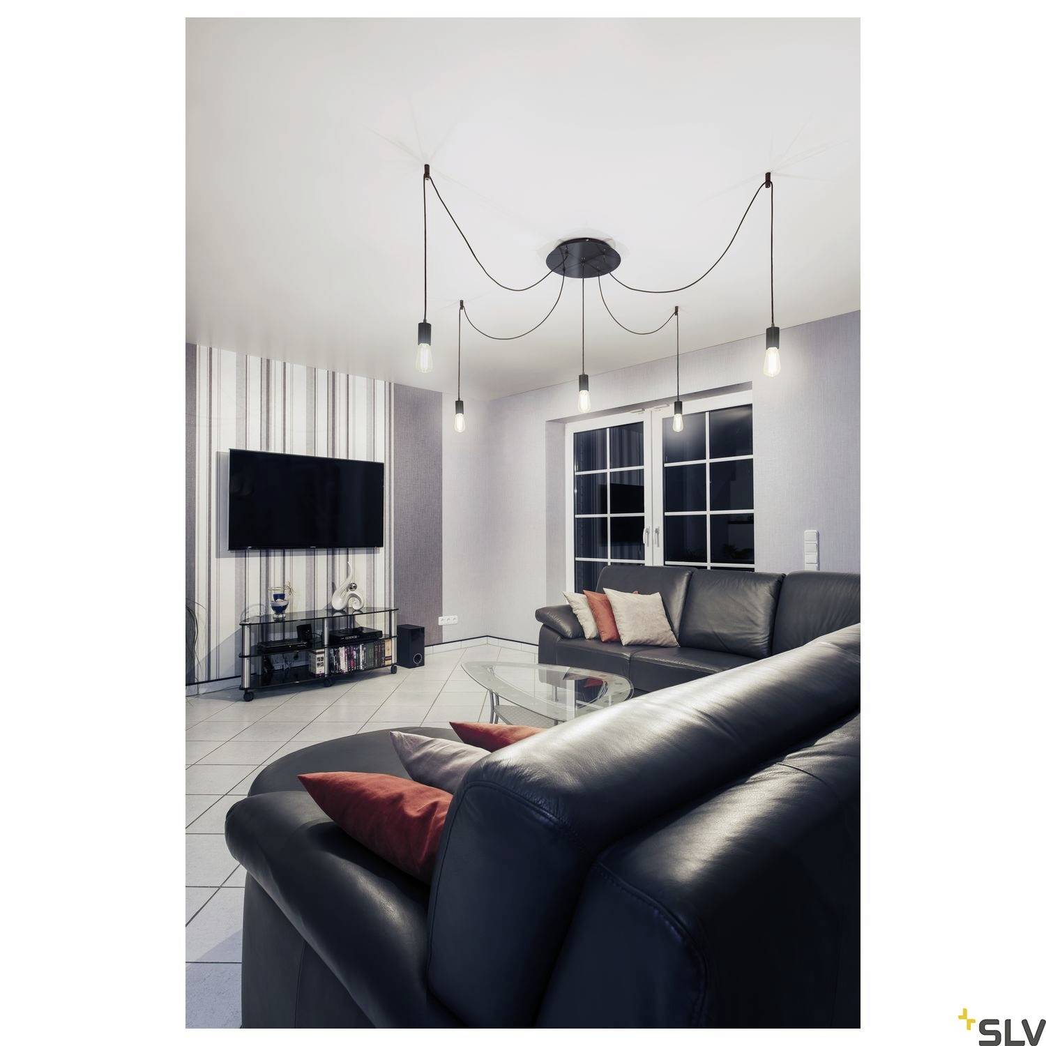 Un salon moderne avec un canapé en cuir, une table basse en verre et une télévision murale. Des luminaires suspendus sont accrochés au plafond. Des fenêtres avec des rideaux sont visibles en arrière-plan.