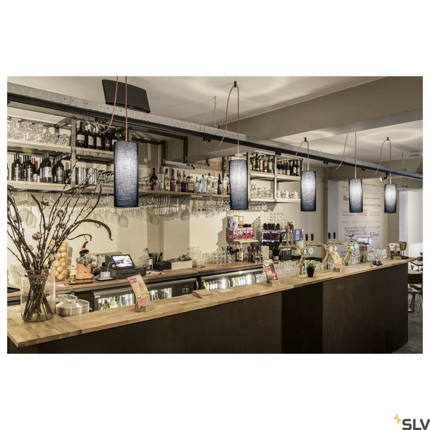 Un bar élégant avec un comptoir éclairé, décoré de branches et de bouteilles. Cinq lampes modernes sont suspendues au-dessus du comptoir.