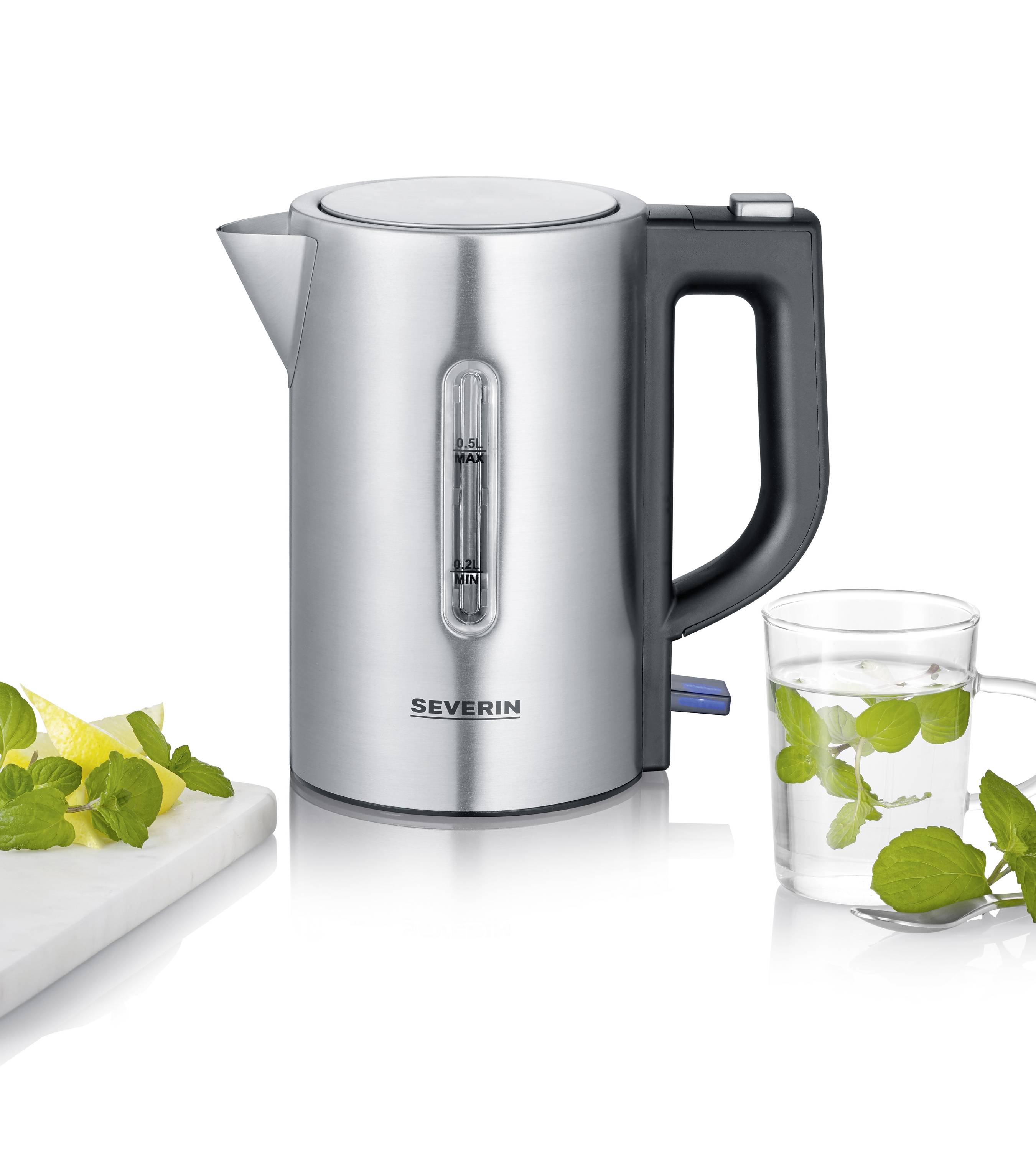 Une bouilloire en acier inoxydable à côté d'un verre d'eau et de feuilles de menthe. Sur une planche se trouvent un citron et d'autres feuilles de menthe.