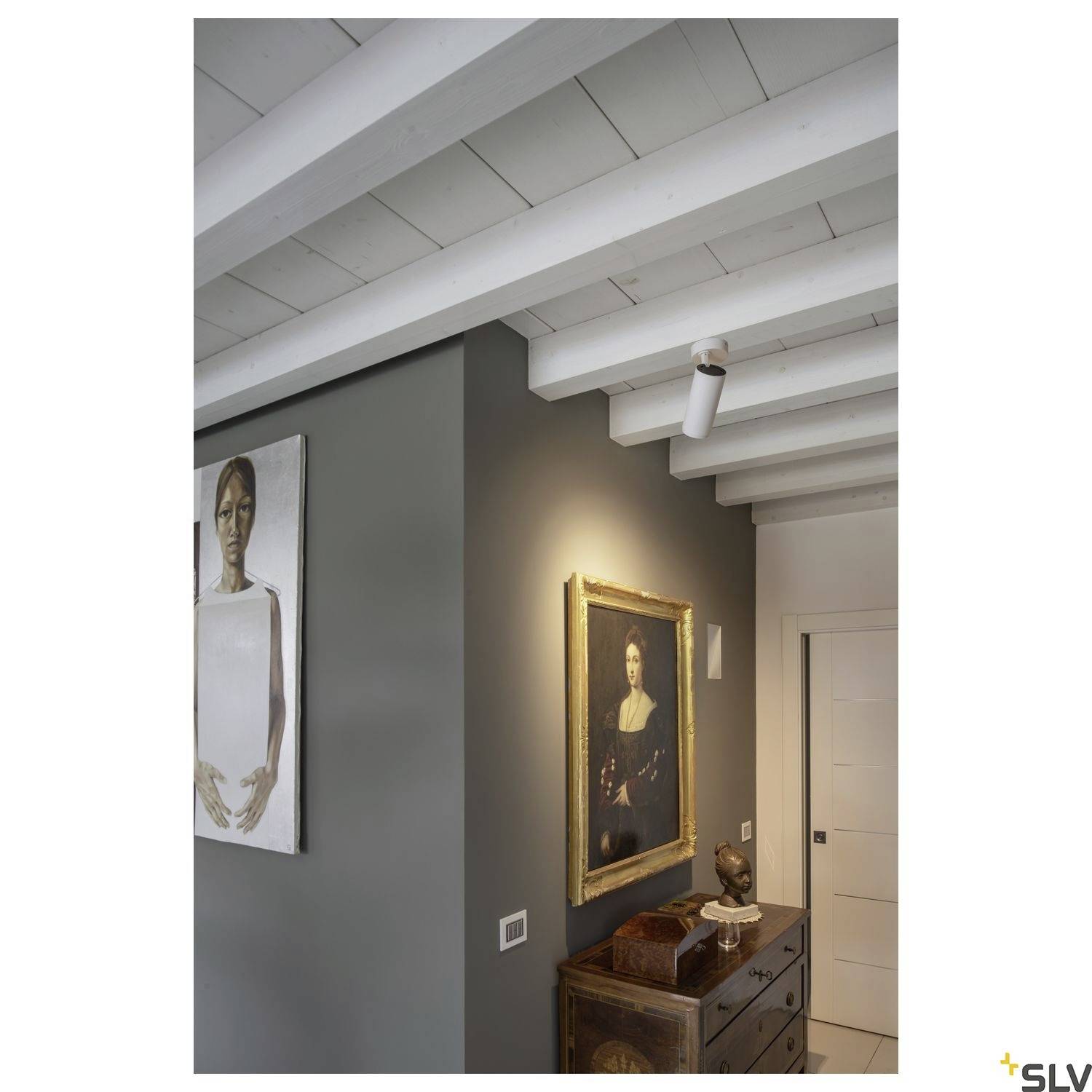 Une pièce avec un plafond à poutres apparentes en bois, des œuvres d'art moderne sur le mur, une peinture classique et une commode ancienne, illustrant une combinaison élégante.