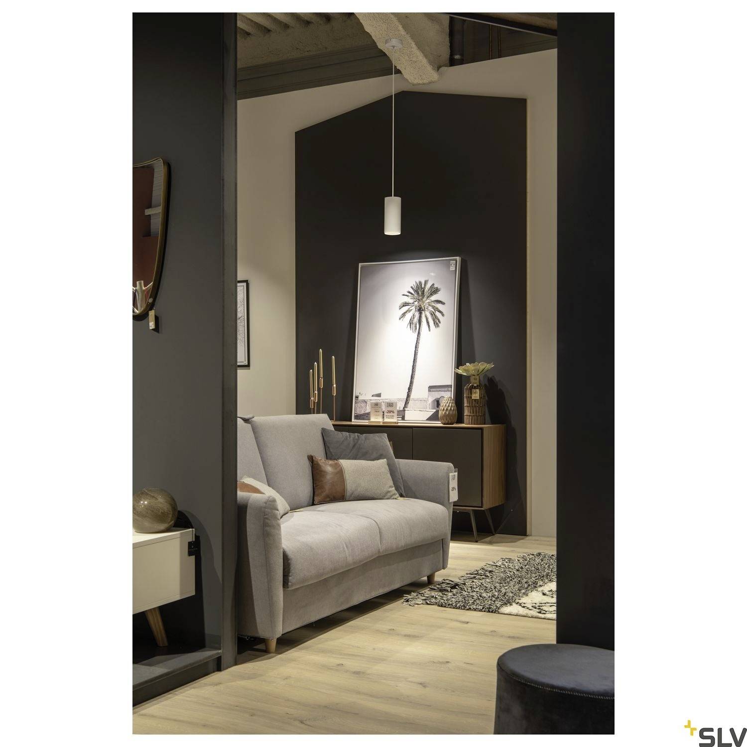 Salon avec un canapé gris, une table d'appoint moderne et un grand tableau de palmier au mur, un éclairage doux crée une ambiance chaleureuse.