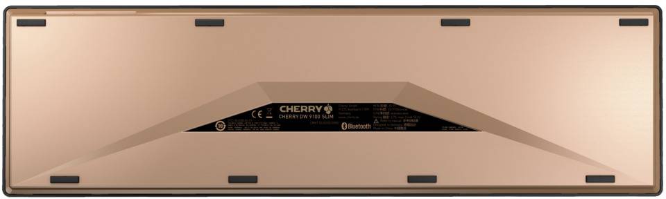 Le dos d'un clavier de couleur cuivre avec le logo 'CHERRY' et le symbole Bluetooth, entouré de pieds en caoutchouc noir pour assurer la stabilité.