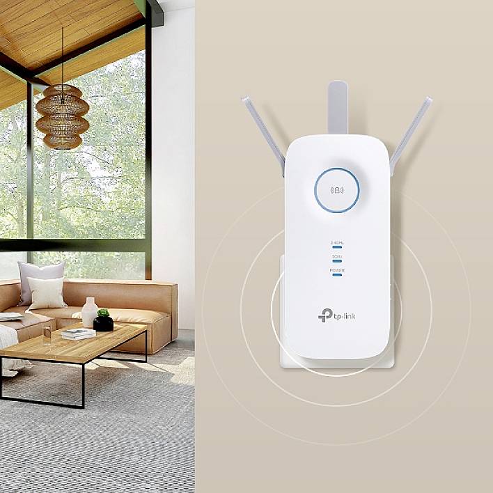 Un amplificateur Wi-Fi de TP-Link avec deux antennes devant un salon lumineux avec un canapé, une grande fenêtre et une table en bois moderne.