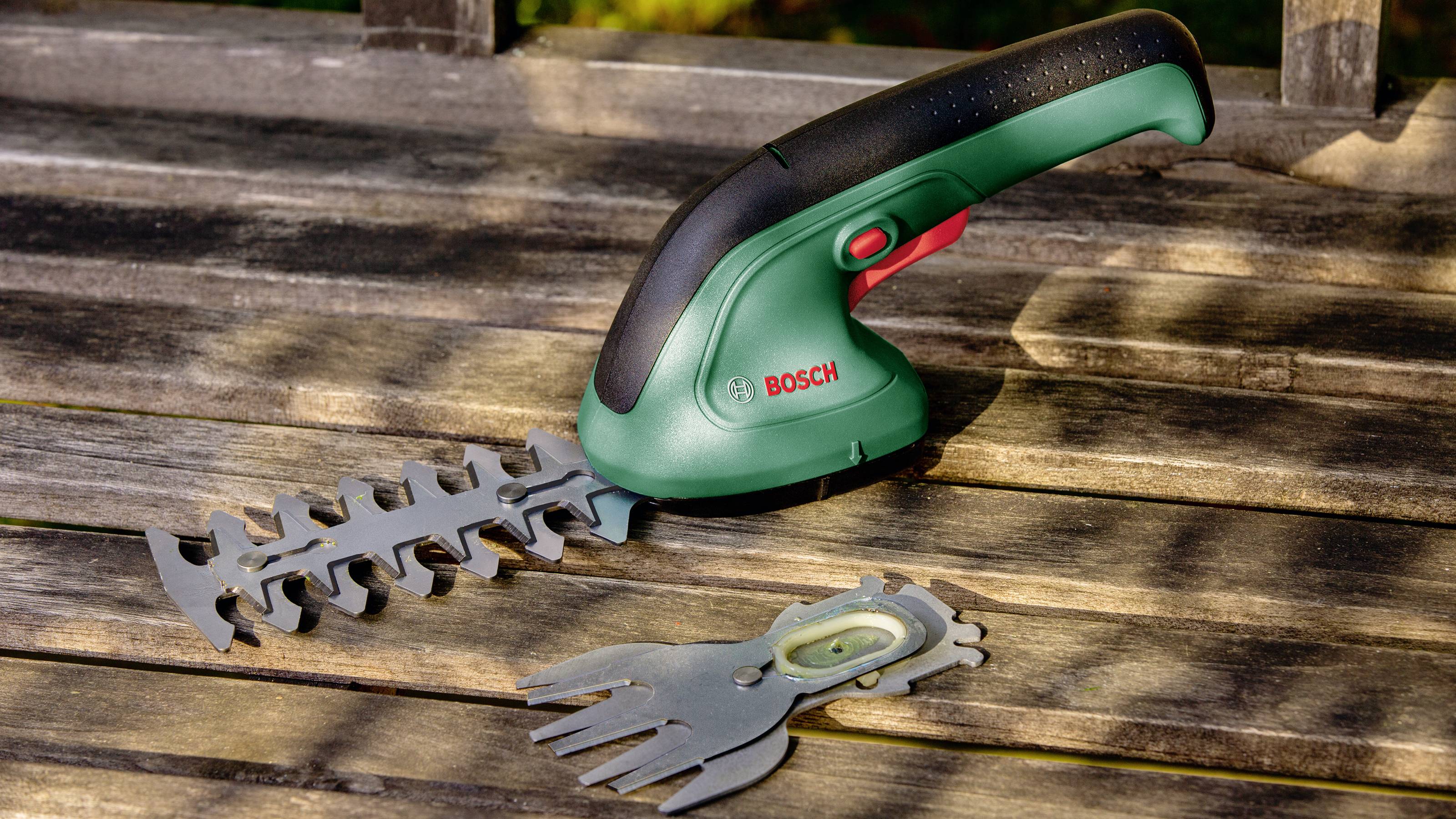 Un taille-haie vert sans fil est posé sur une table en bois à côté d'un embout de lame interchangeable.
