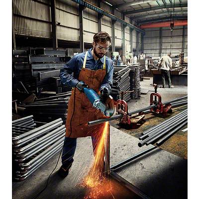 Un homme coupe des tubes métalliques avec une meuleuse d'angle dans un atelier. Des étincelles volent, l'environnement est rempli de matériaux en acier.