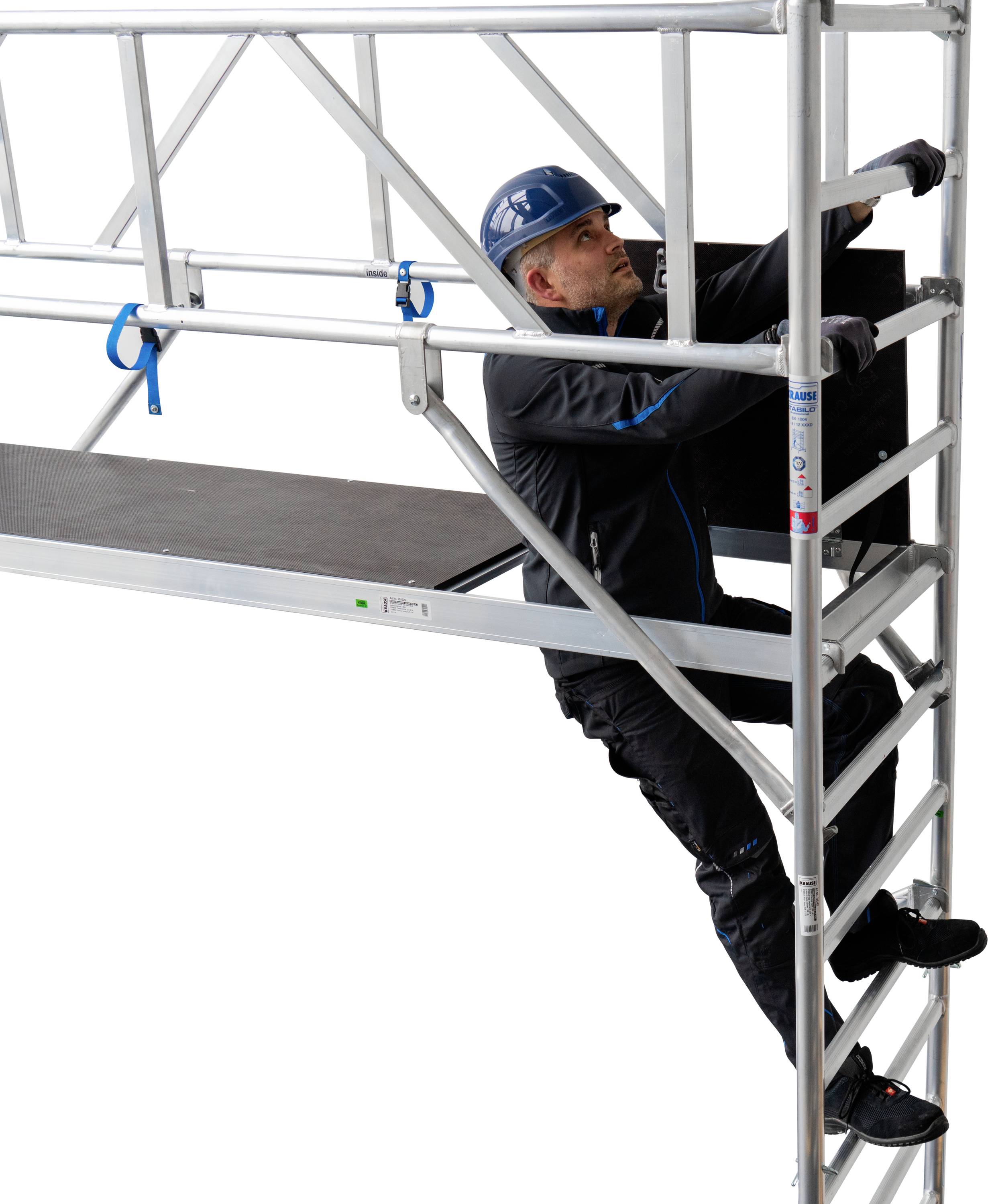 Un ouvrier gravit une échelle en aluminium sur un échafaudage, portant un casque bleu et des vêtements de travail noirs.