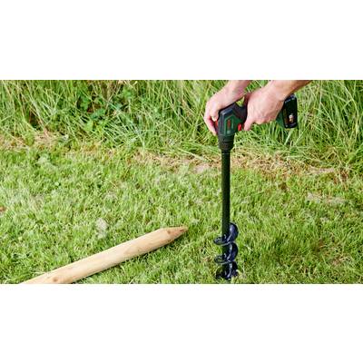 Une personne utilise une perceuse sans fil avec un embout tarière pour percer un trou dans une surface d'herbe verte. Un pieu en bois est posé à côté.