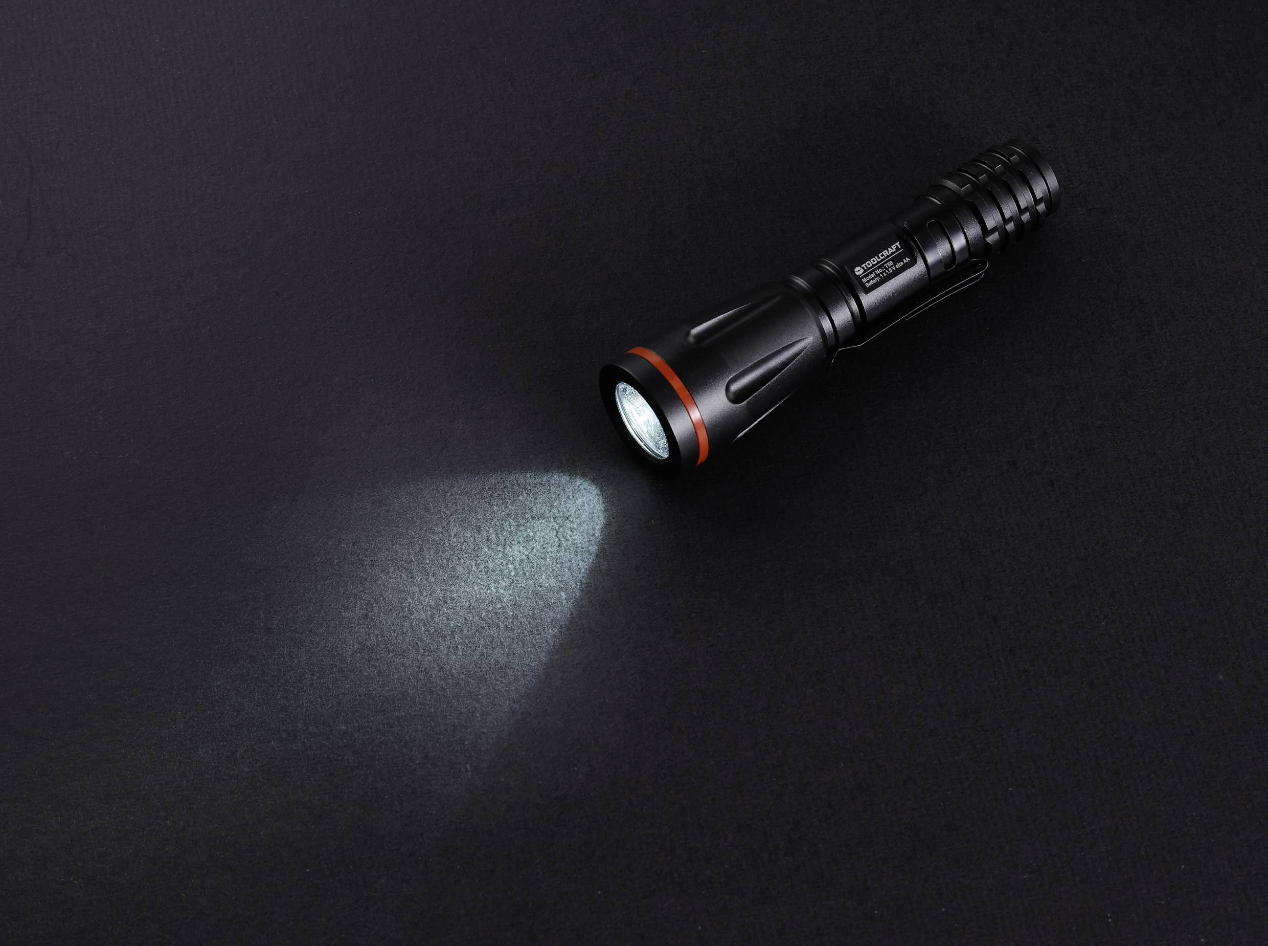 Une lampe de poche noire brille sur une surface sombre.