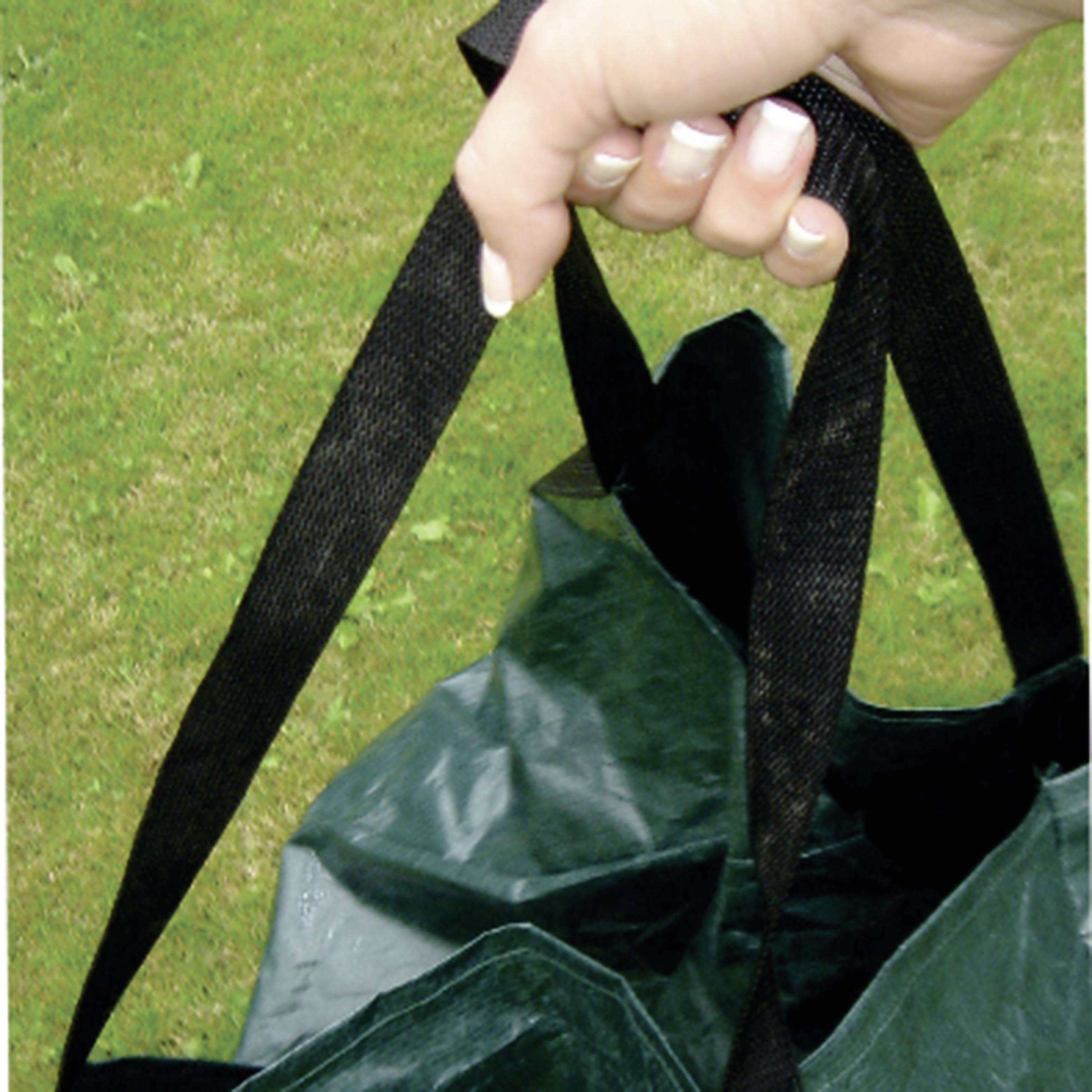 Une main tient un sac vert avec des poignées noires. L'arrière-plan montre une pelouse verte.