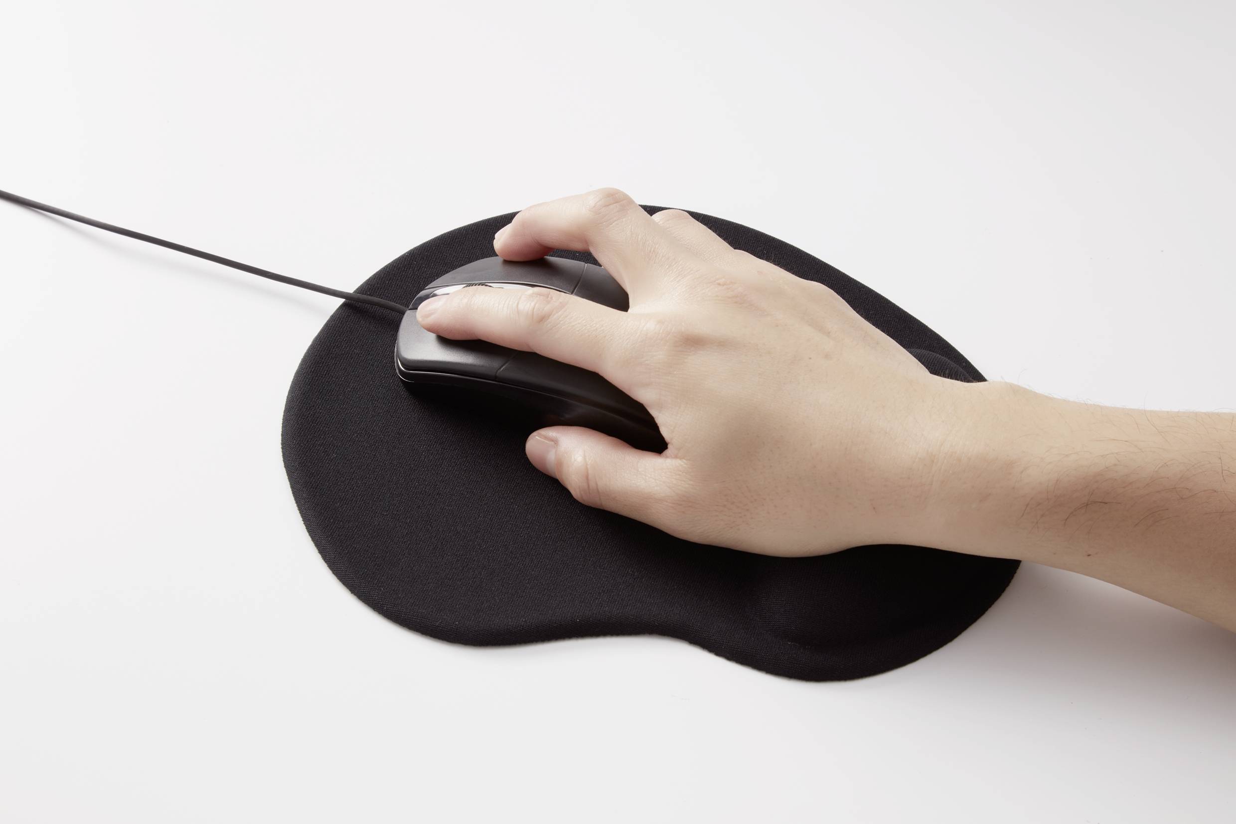 Une main tient une souris d'ordinateur posée sur un tapis de souris noir.