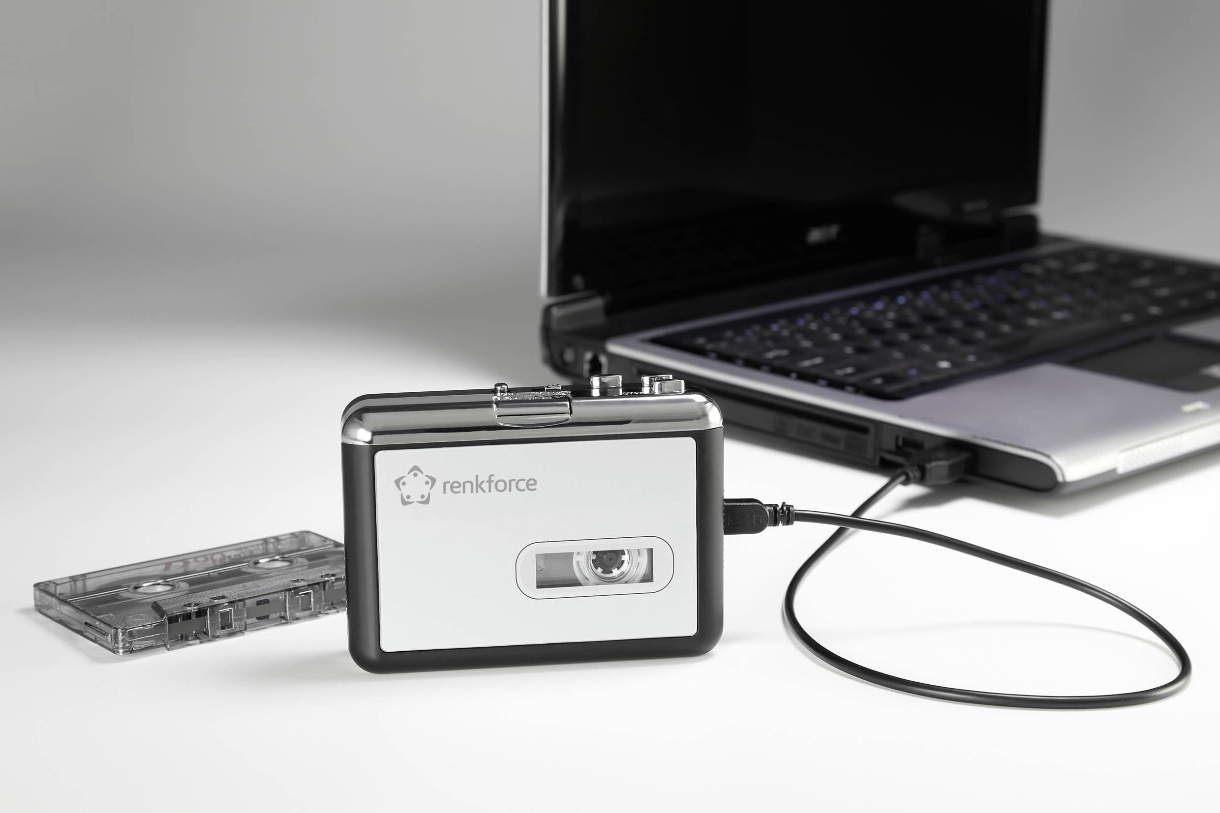 Lecteur de cassettes 'renkforce', connecté à un ordinateur portable. Une cassette est posée à côté. L'ordinateur portable est allumé.