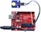 Carte de microcontrôleur rouge avec port USB et module de capteur à LED bleue, connectés par des câbles, montrant un circuit électronique.