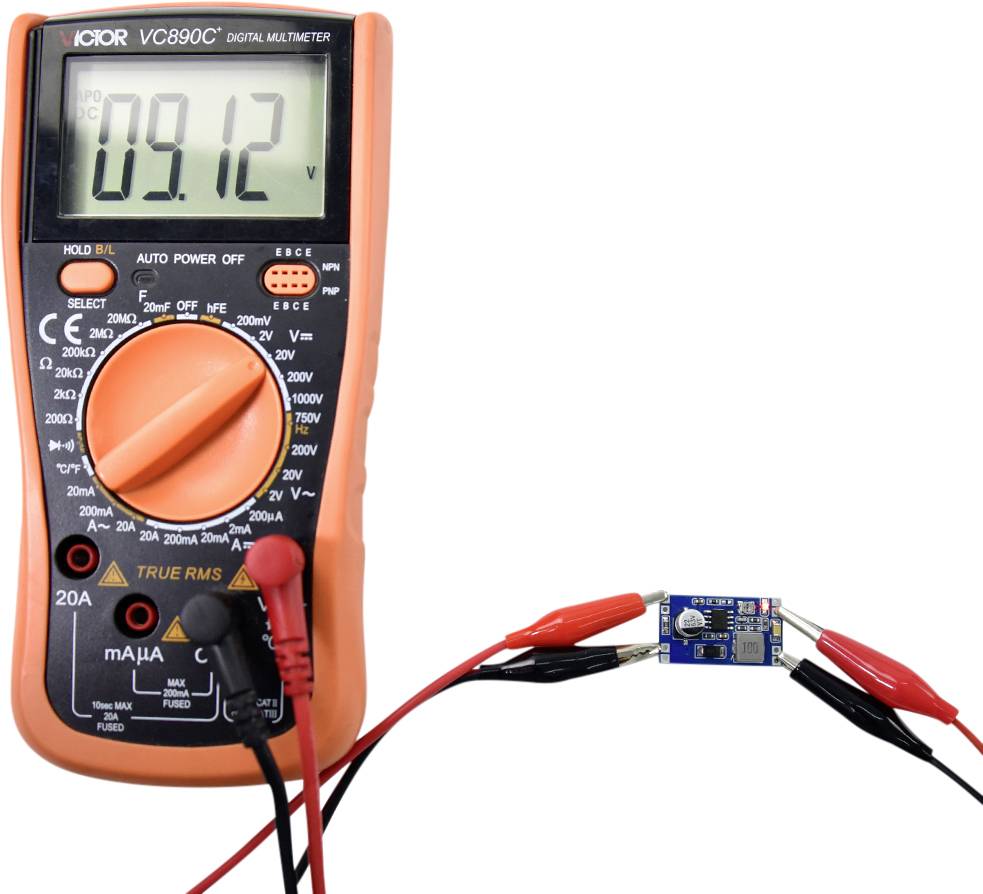 Un multimètre numérique affiche '09,12'. Il est connecté à un circuit électronique et mesure la tension.
