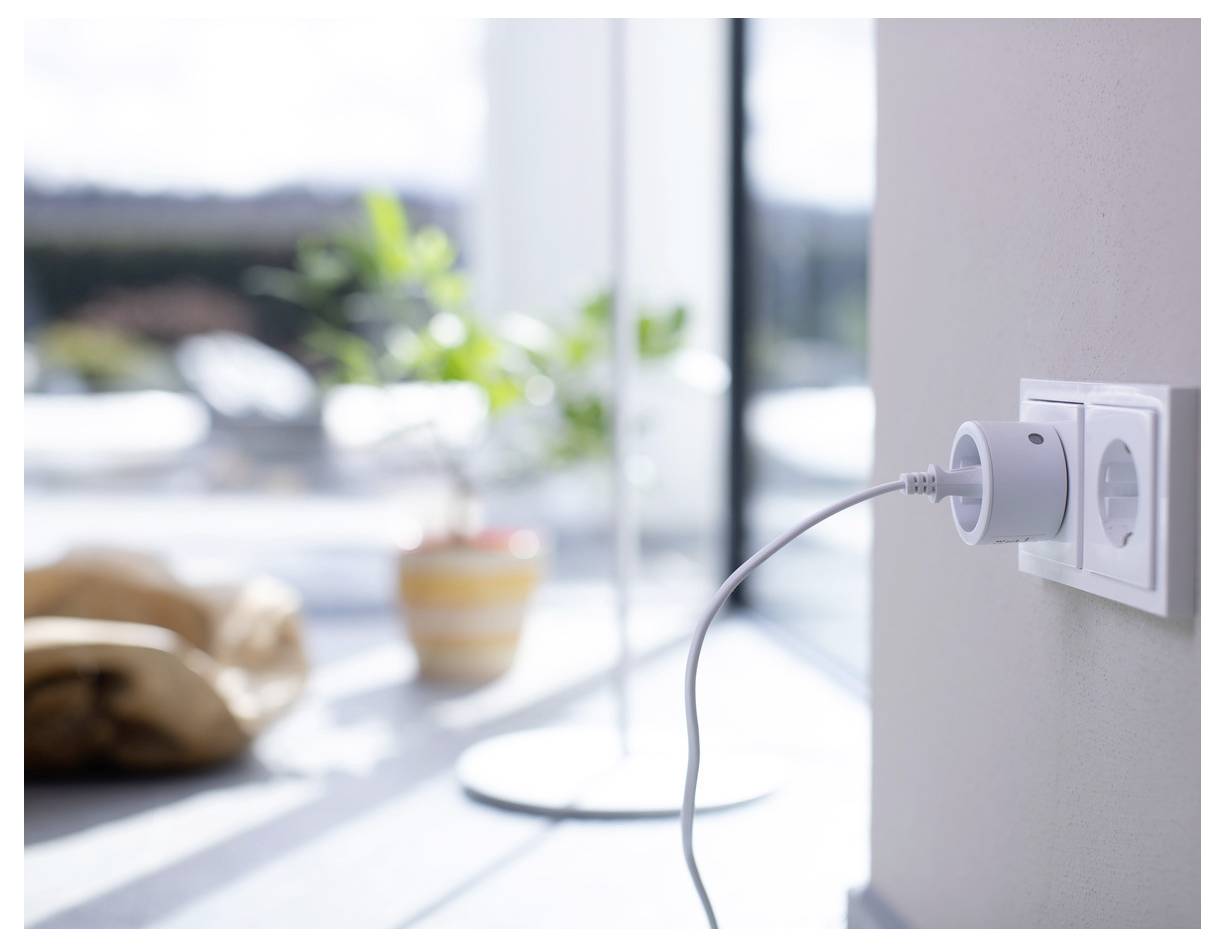 Prise de courant blanche avec un chargeur branché, câble pendant vers le bas dans une pièce ensoleillée et lumineuse.